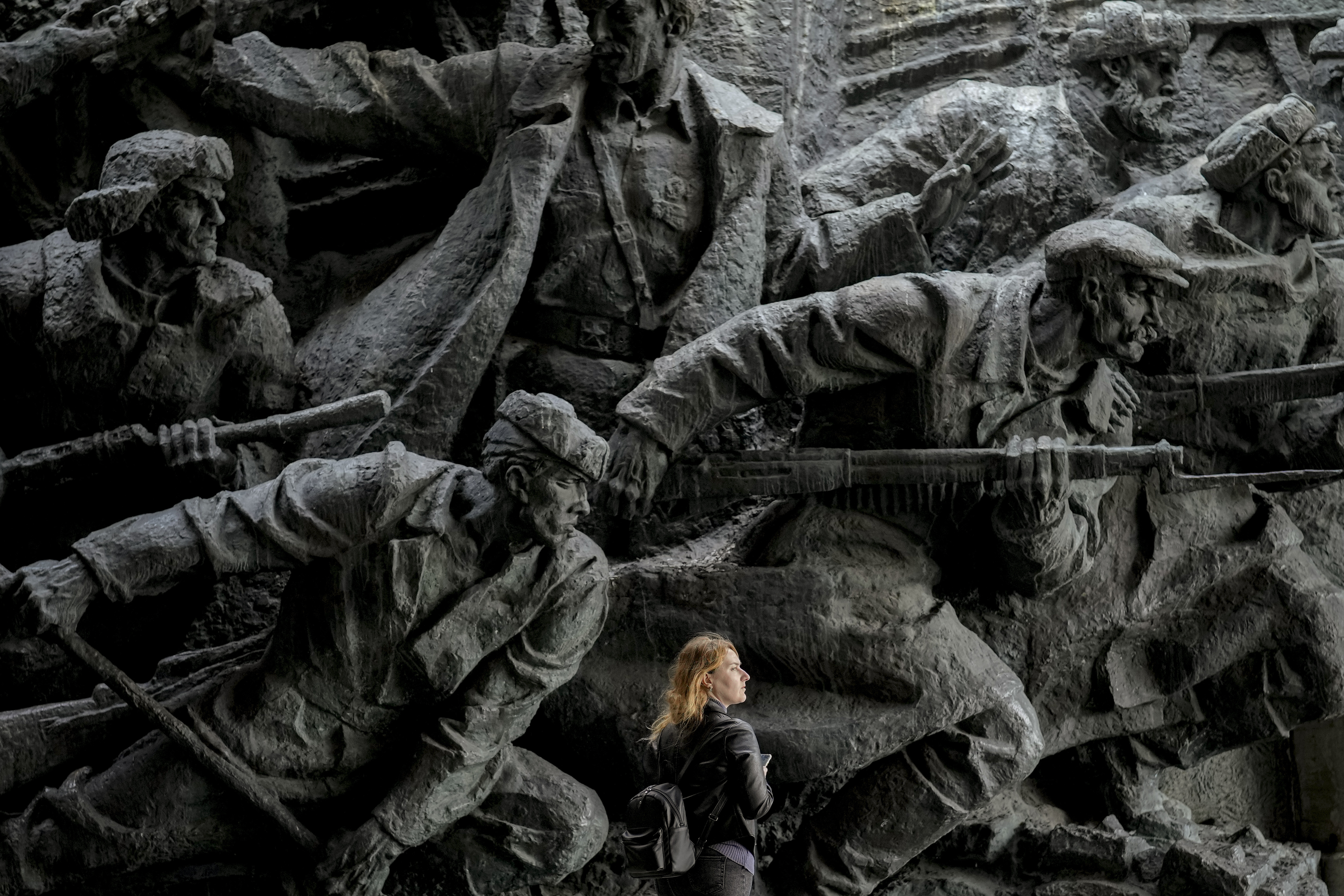 A woman walking in front of bas-relief sculptures depicting war scenes in the National Museum of the History of Ukraine in the Second World War in Kyiv. She looks tiny in comparison with the sculptures.