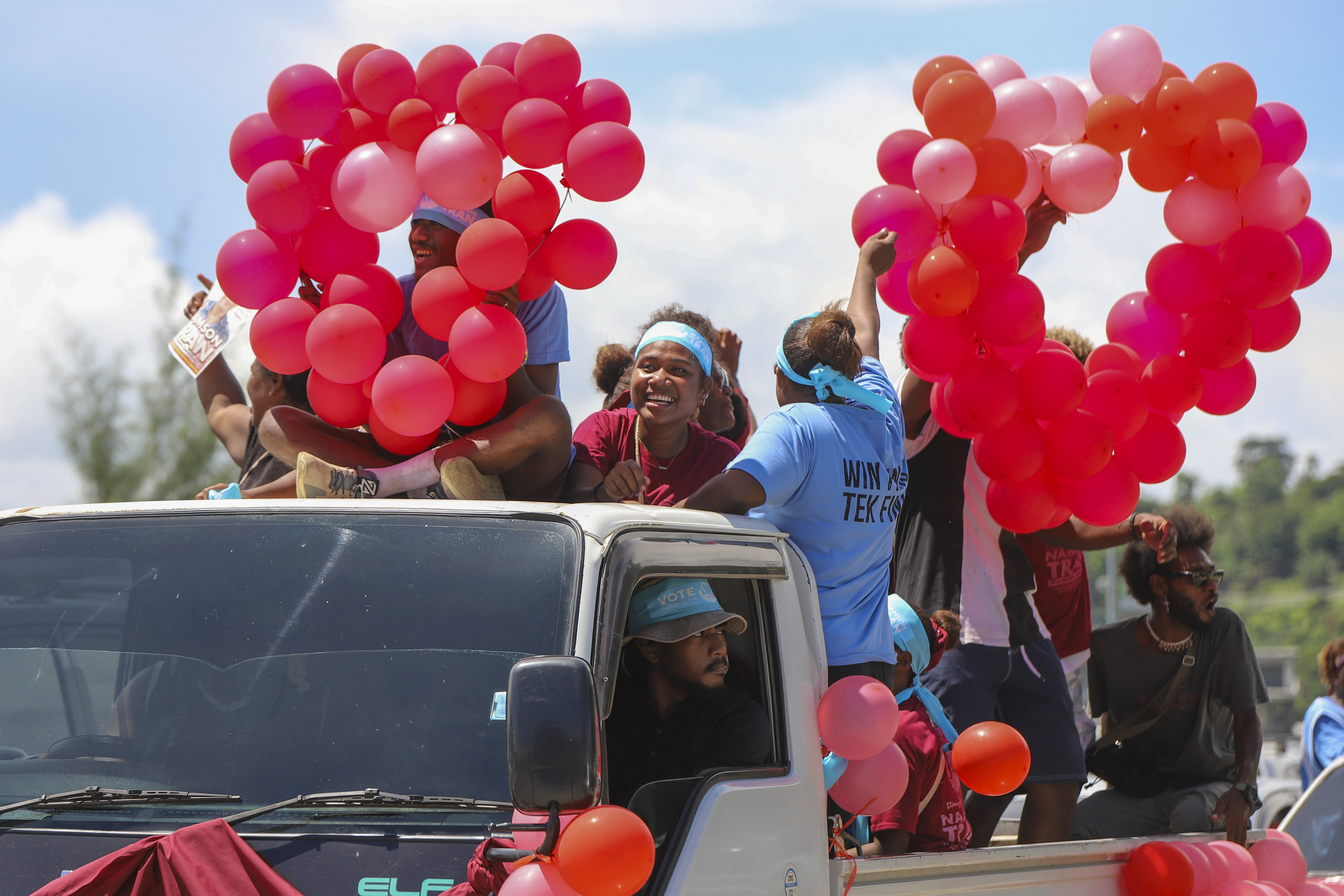 People in Solomon Islands holding red balloons at a campaign rally. They're crowded on the back of a small lorry.