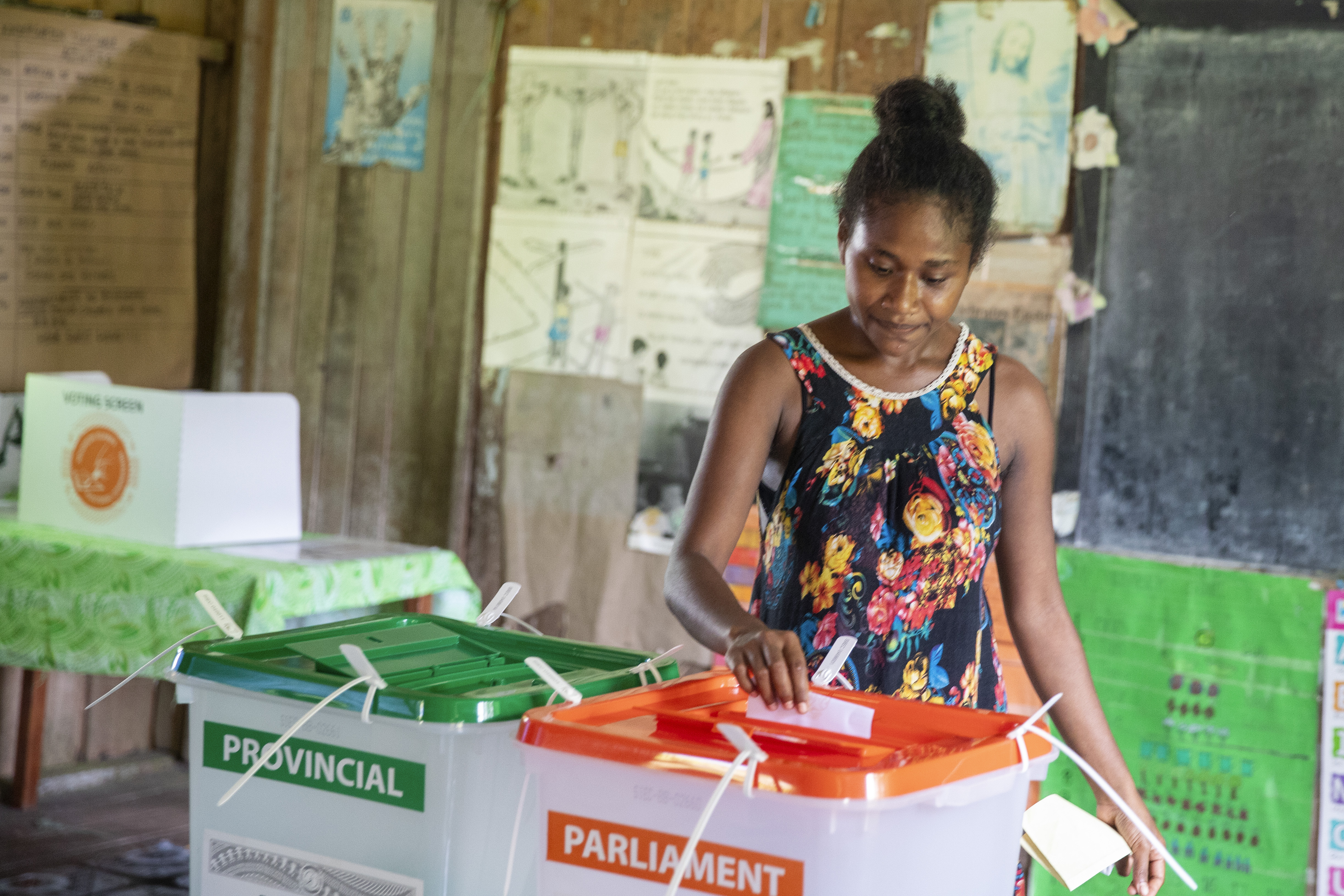 A woman in the Solomon Islands casting her ballot. The clear box for the parliamentary election has an orange lid while the one for the provincial poll has a green lid.