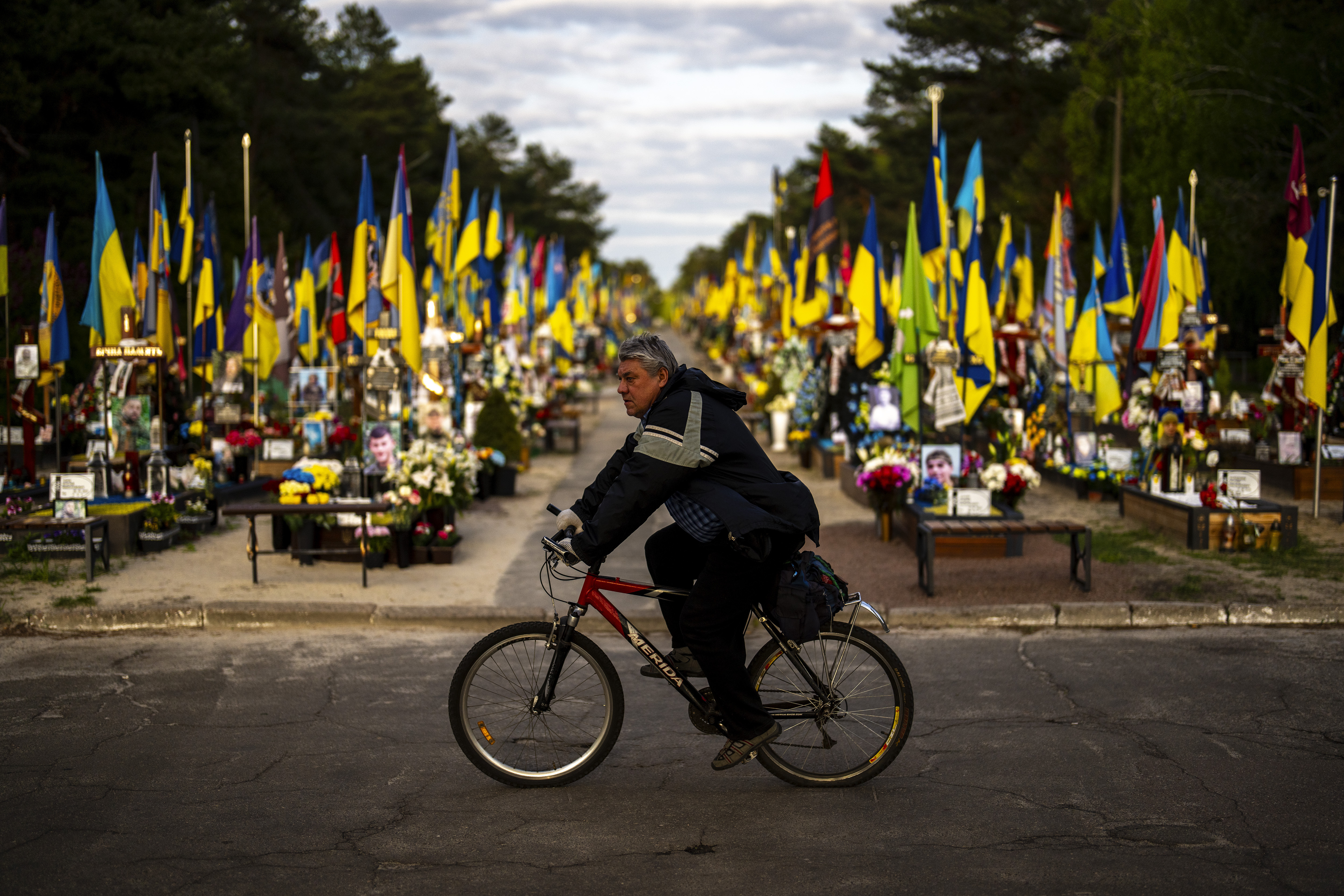 A man rides a bicycle past the tombs of Ukrainian soldiers killed during the war, at Lisove cemetery in Kyiv, Ukraine, Tuesday, April 23