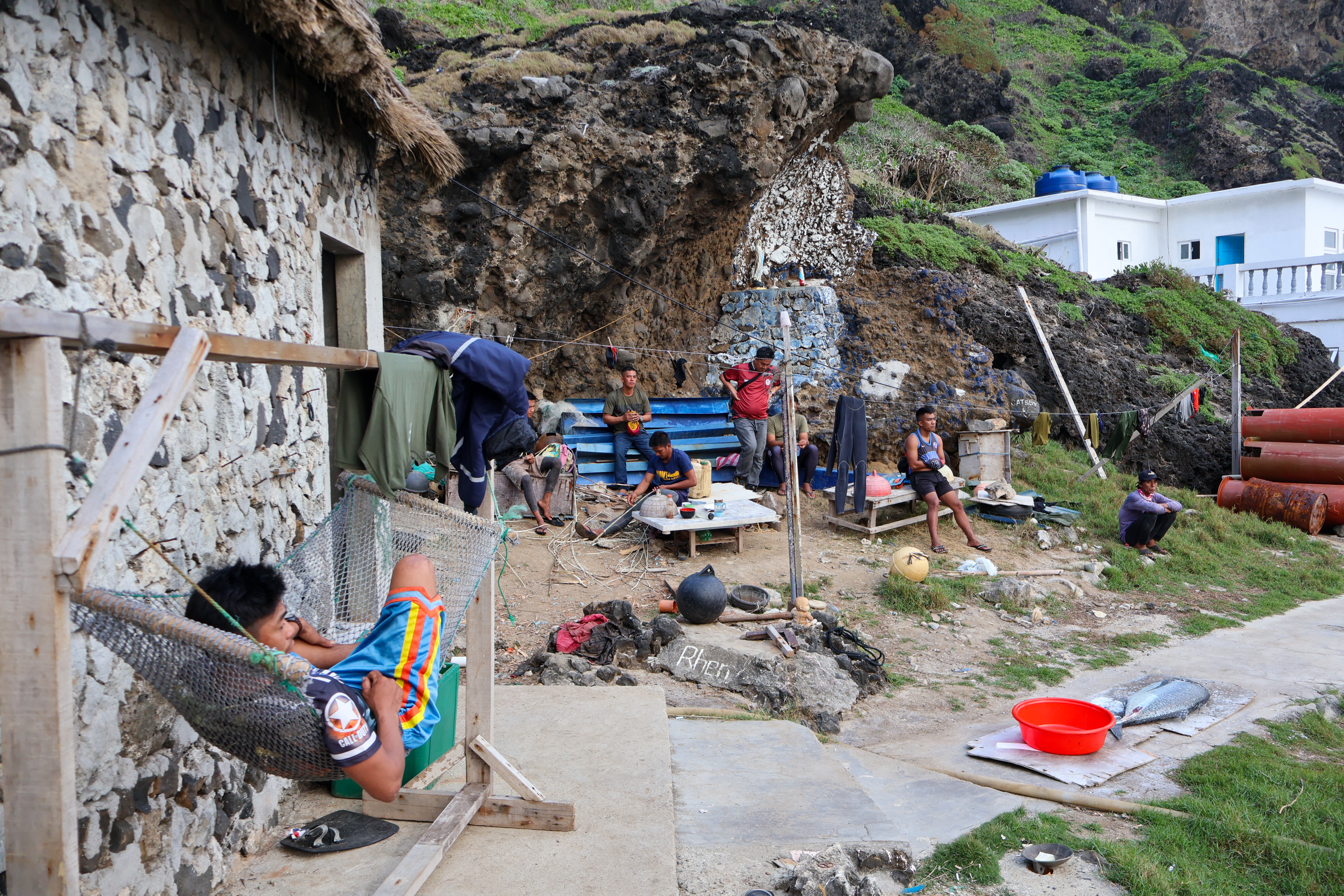 Soldiers hanging out on Mavulis. Their quarters are to the left. One is lying in a hammock. Others are tending the garden or looking at their phones.