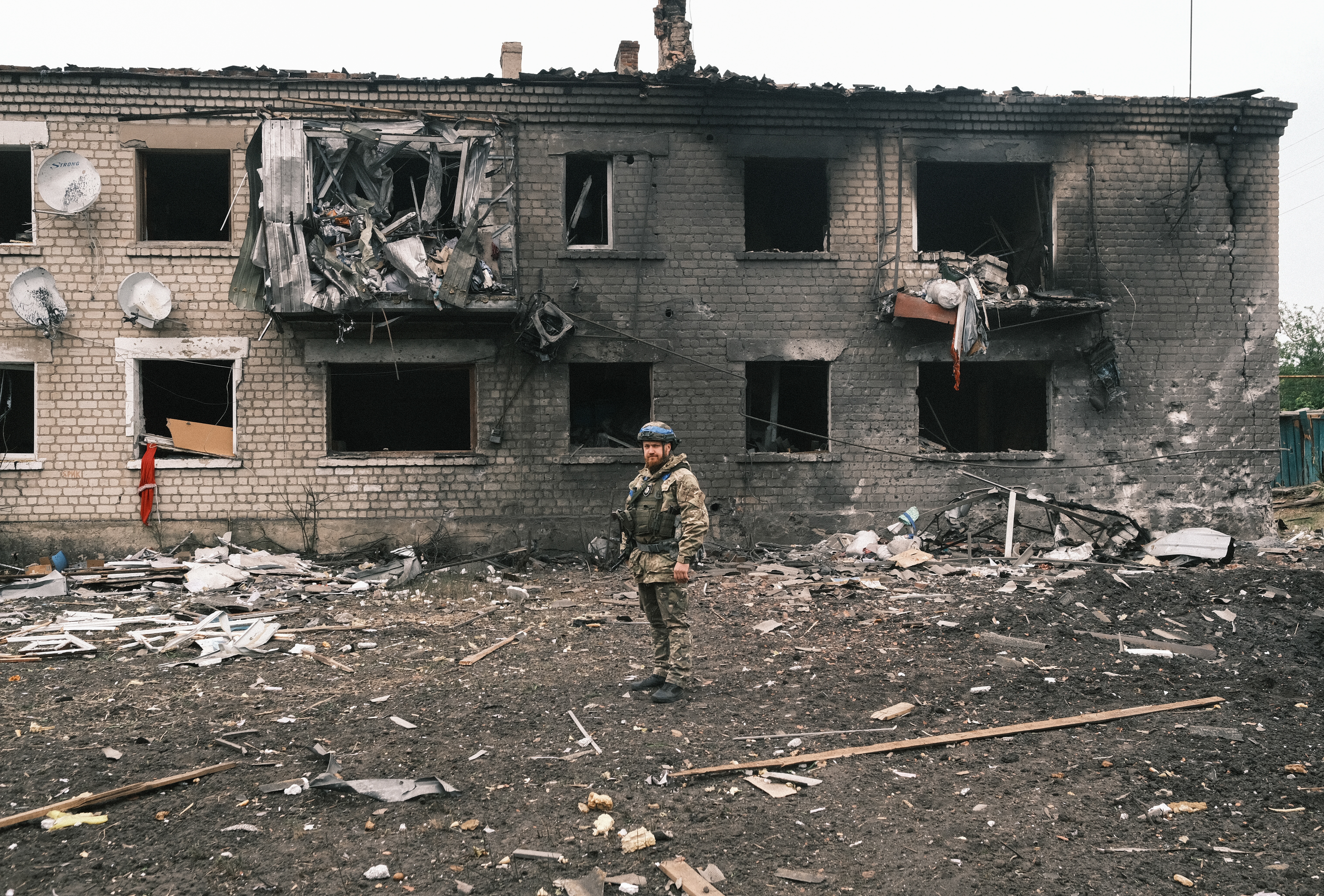 A Ukrainian police officer standing in front of a blackened damaged building in Vovchansk. The building's windows are all missing.