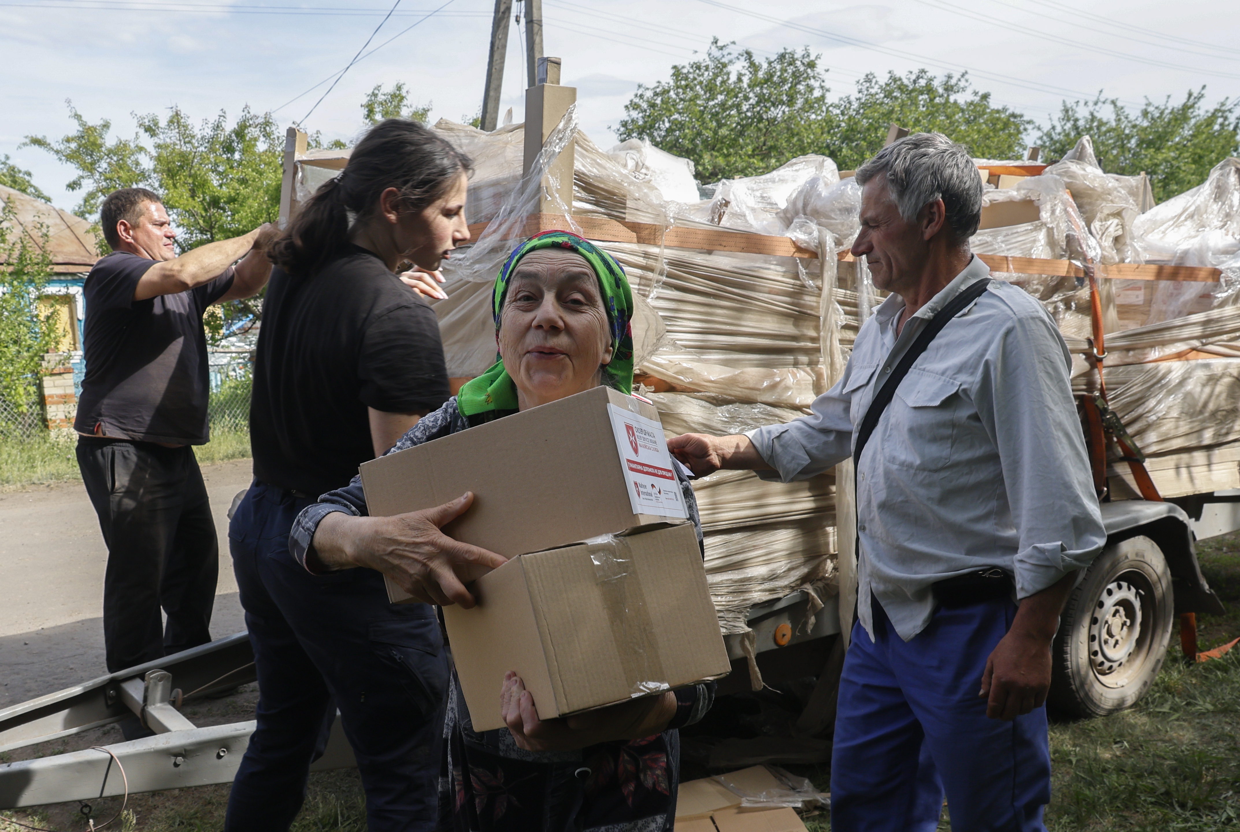A Ukrainian woman carrying boxes of assistance provided by volunteers. More people are queuing behind her.