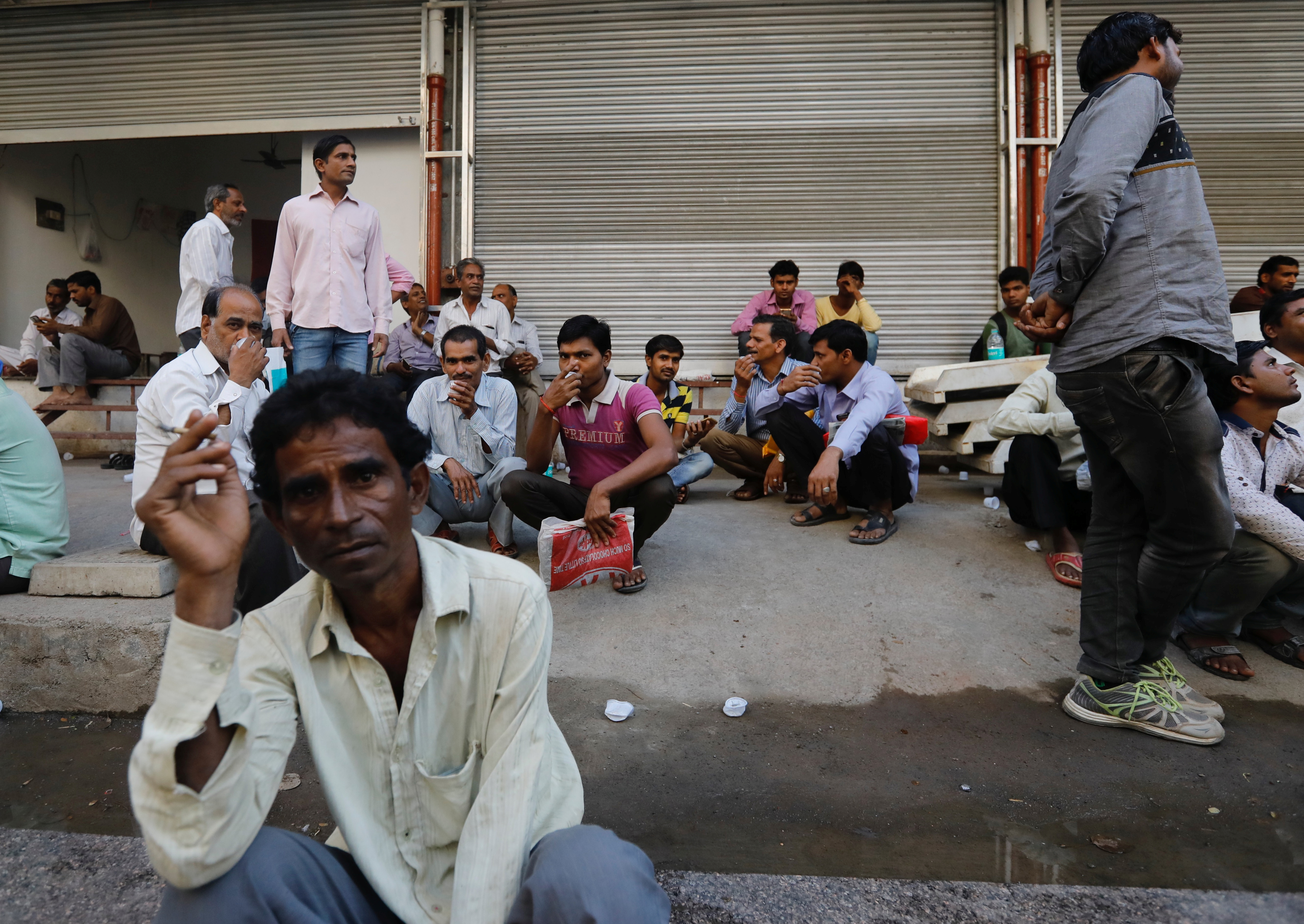 Tradespeople sit on the side of a road as they wait to get hired for work in Mumbai, India