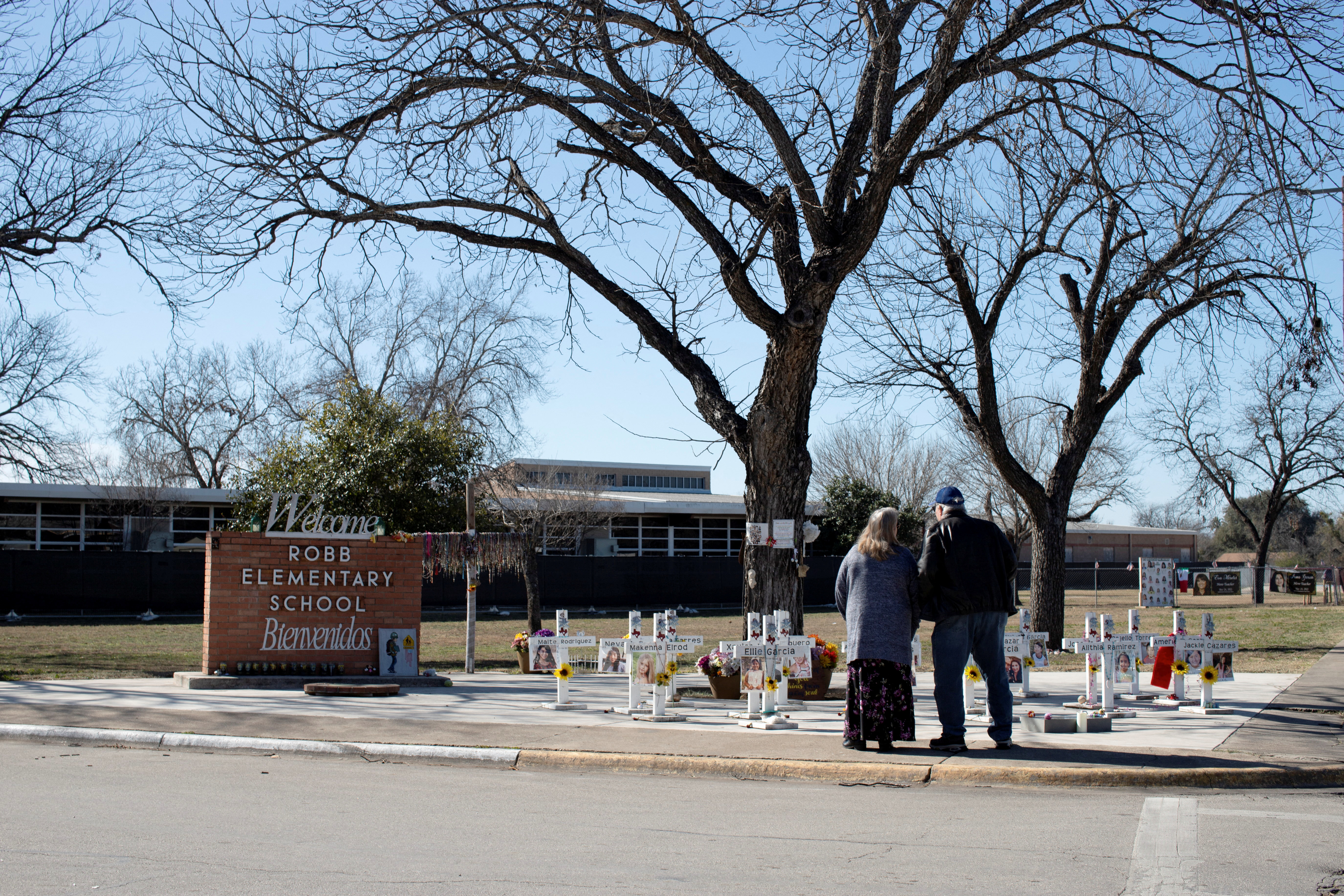A pair of people stand beside a memorial with crosses erected for the victims of the Uvalde school shooting.