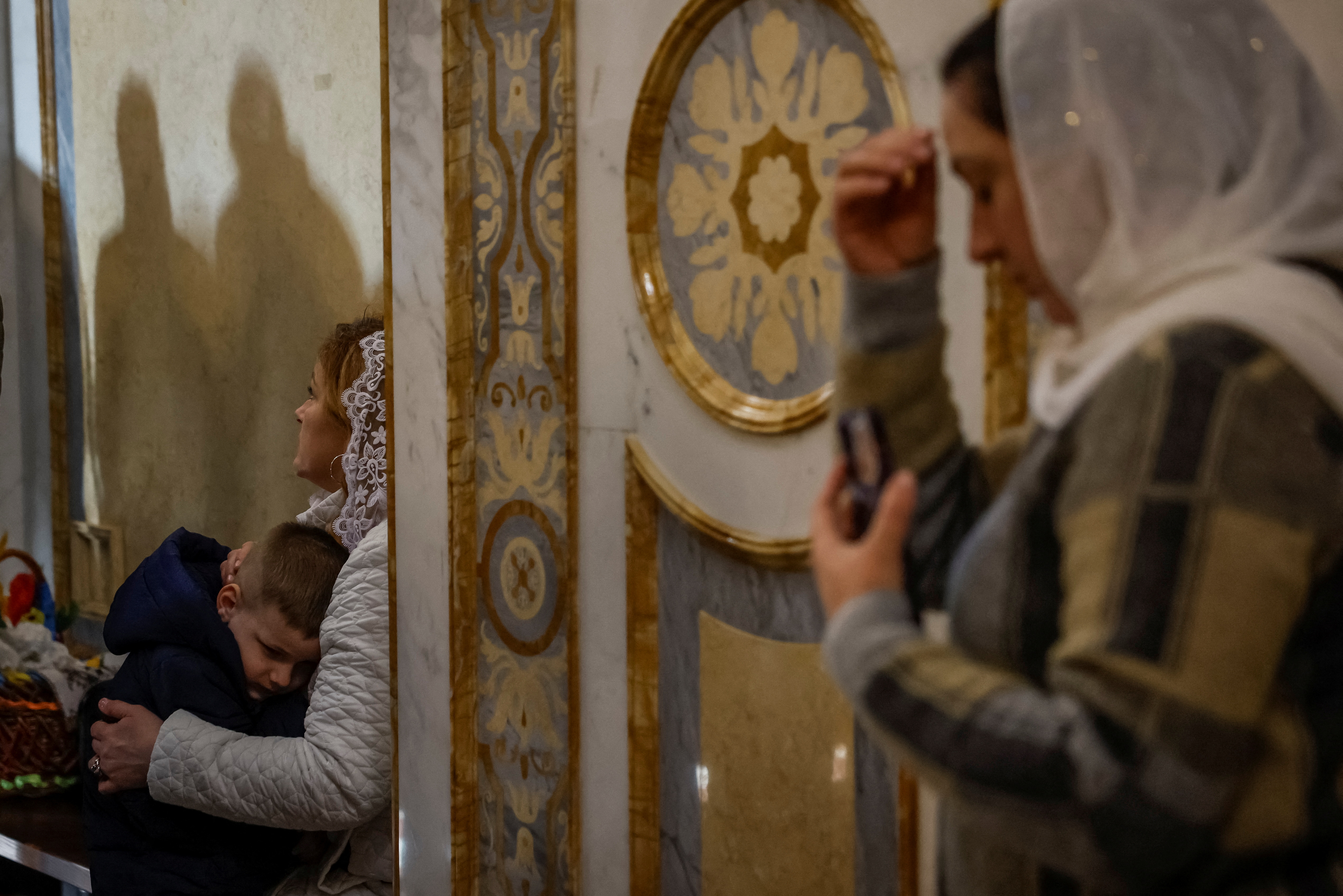 A woman holds his son while other believers pray during an Easter service in a church at a compound of the Kyiv Pechersk Lavra monastery, amid Russia's attack on Ukraine, in Kyiv,