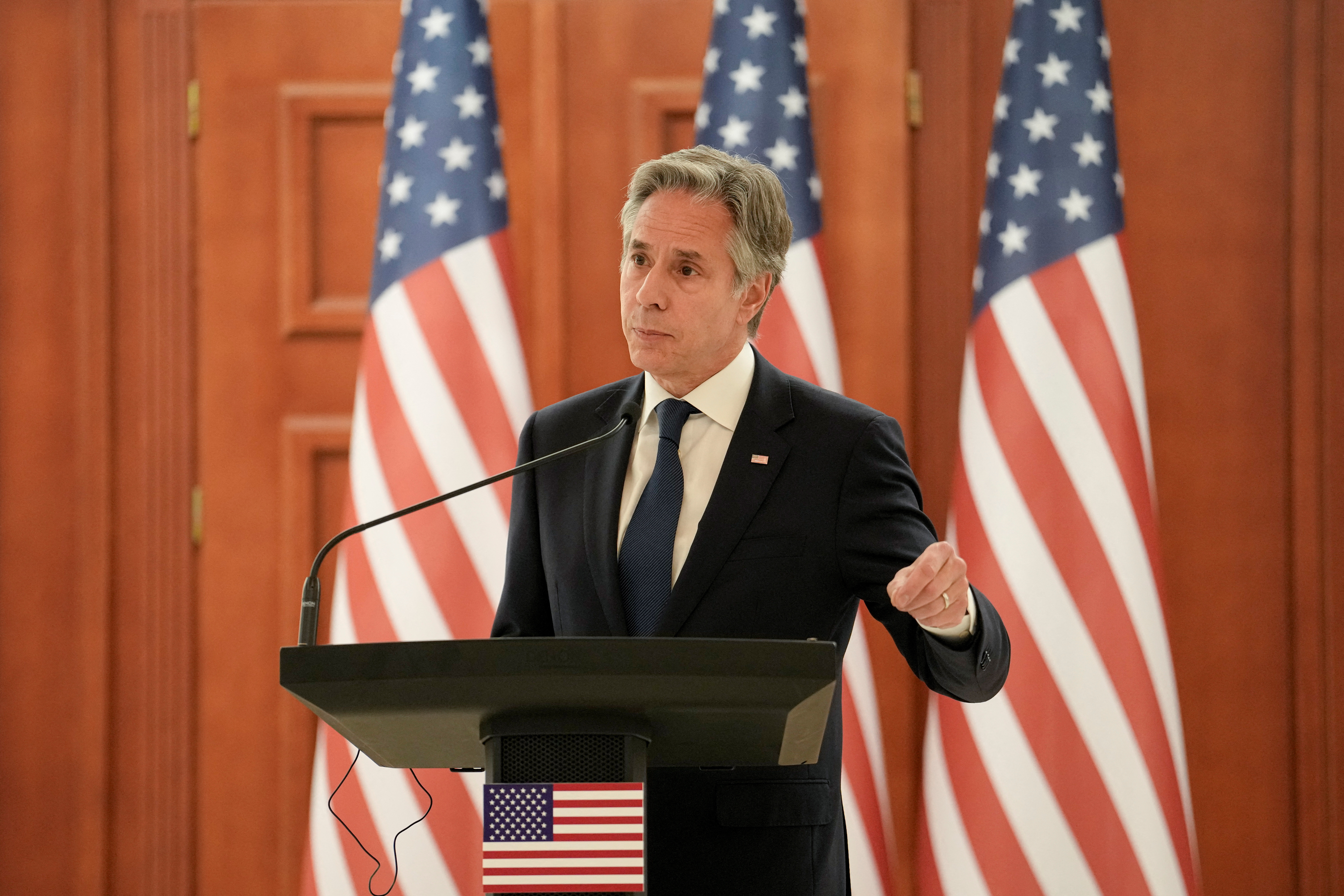 Antony Blinken with three US flags behind him