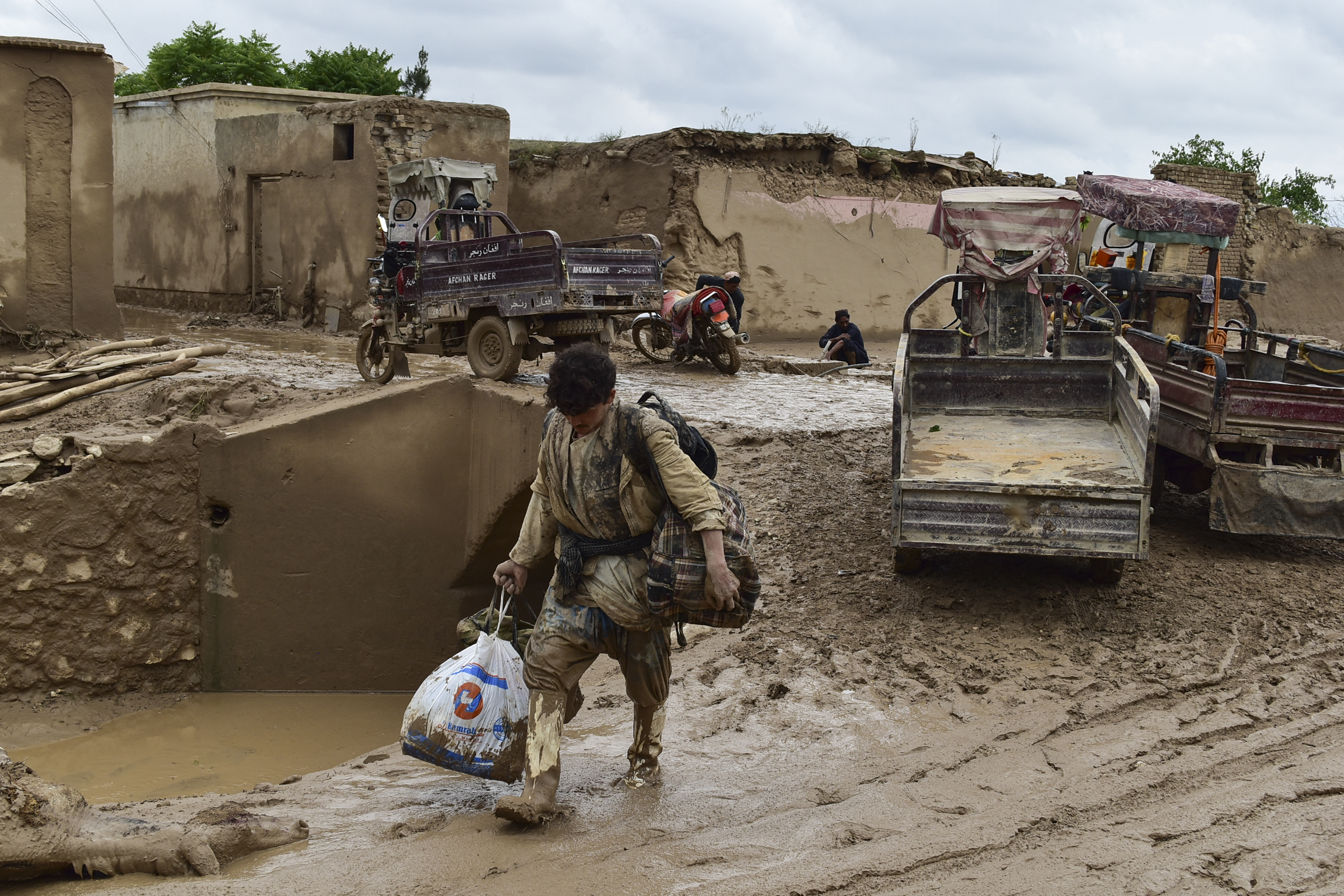 An Afghan man carries his belongings as he walks through a mud covered street following a flash flood after a heavy rainfall in Laqiha village of Baghlan-i-Markazi district in Baghlan province on May 11, 2024. At least 62 people, mainly women and children, were killed on May 10 in flash flooding that ripped through Afghanistan's Baghlan province, in the north of the country, a local official told AFP. (Photo by AFP)