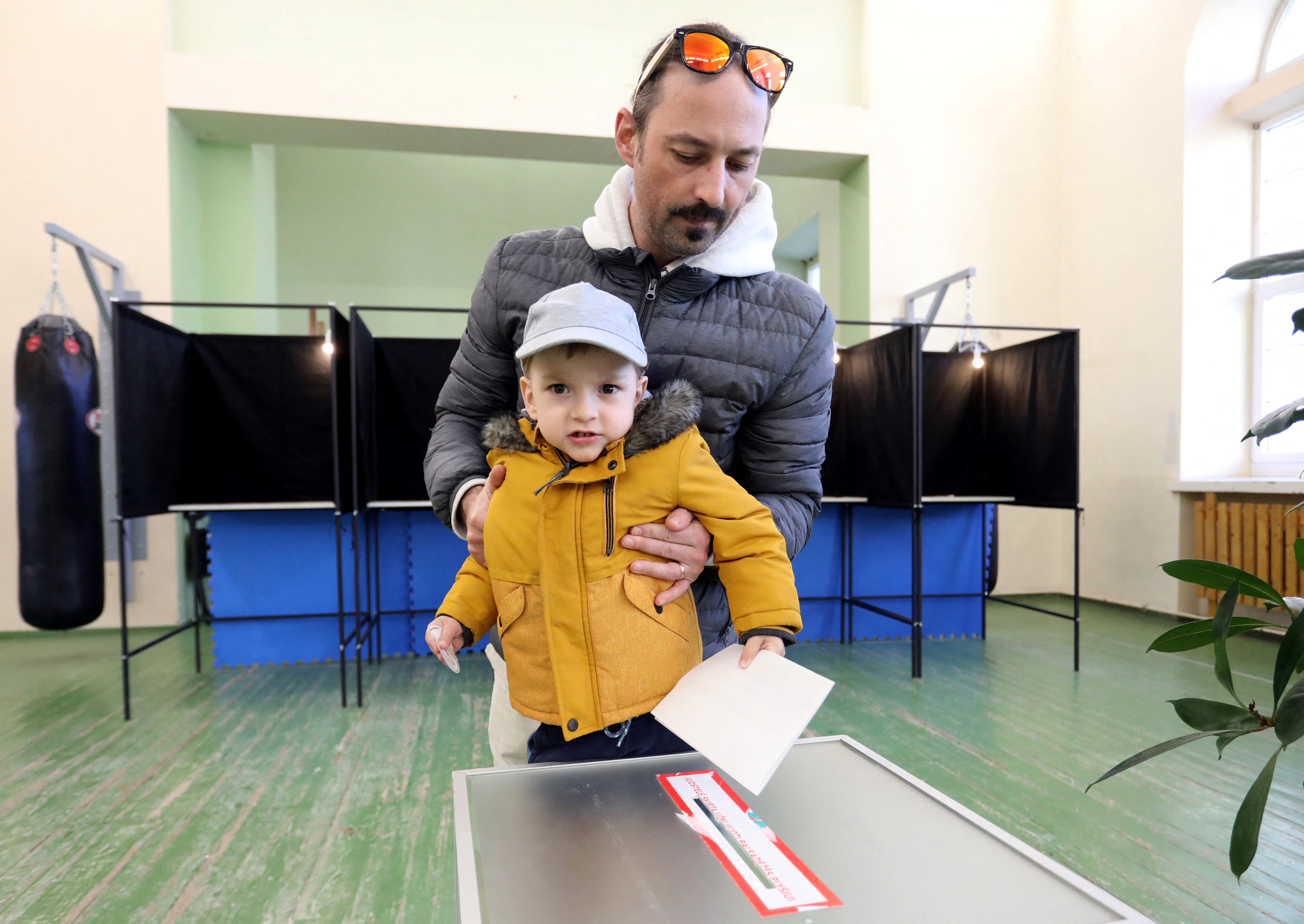 A voter with child prepares to cast a ballot into an urn during the first round of Lithuania's presidential election at a polling station in Vilnius