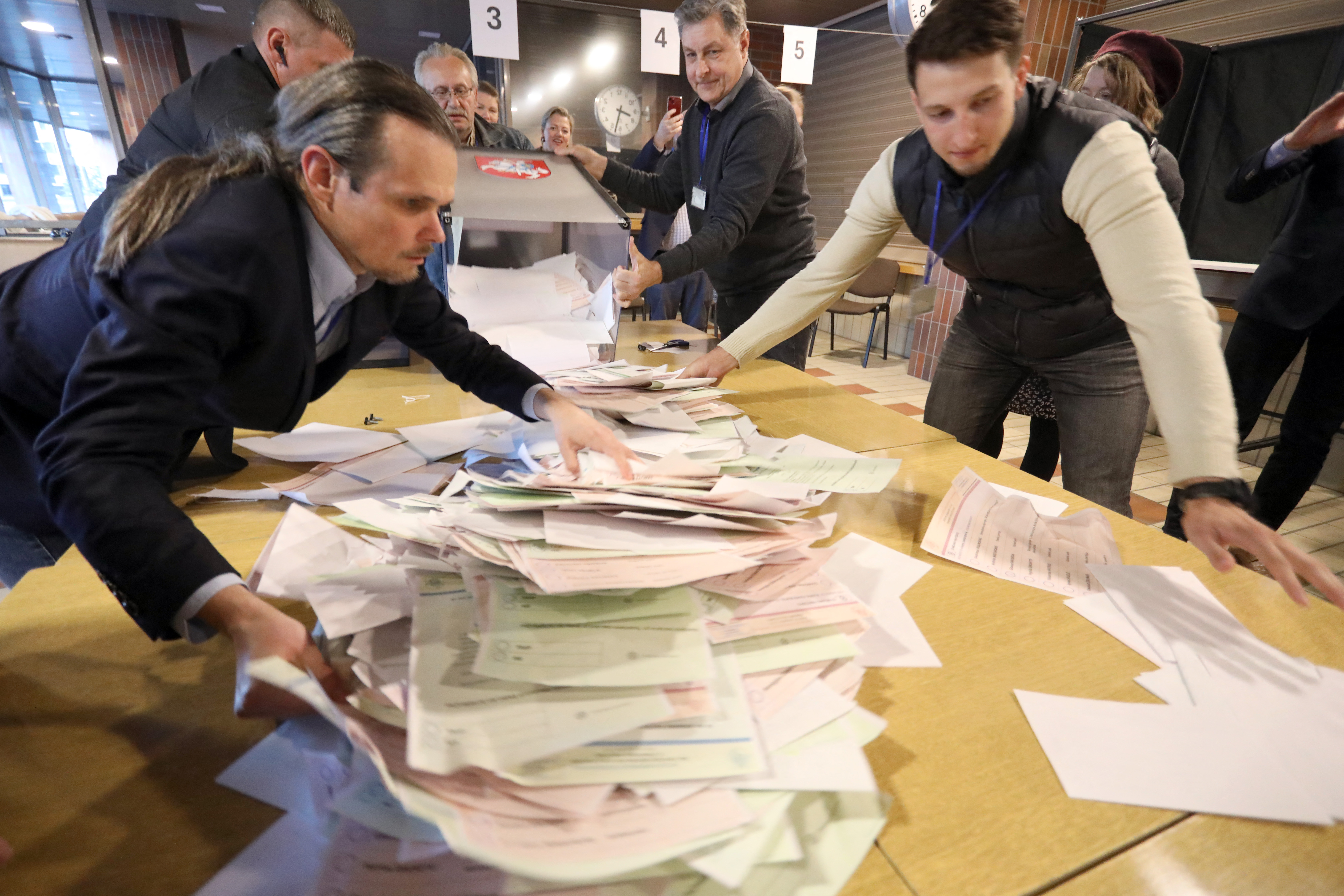Election officials empty a ballot box onto a table. There is a big pile of ballot papers that they are organising.