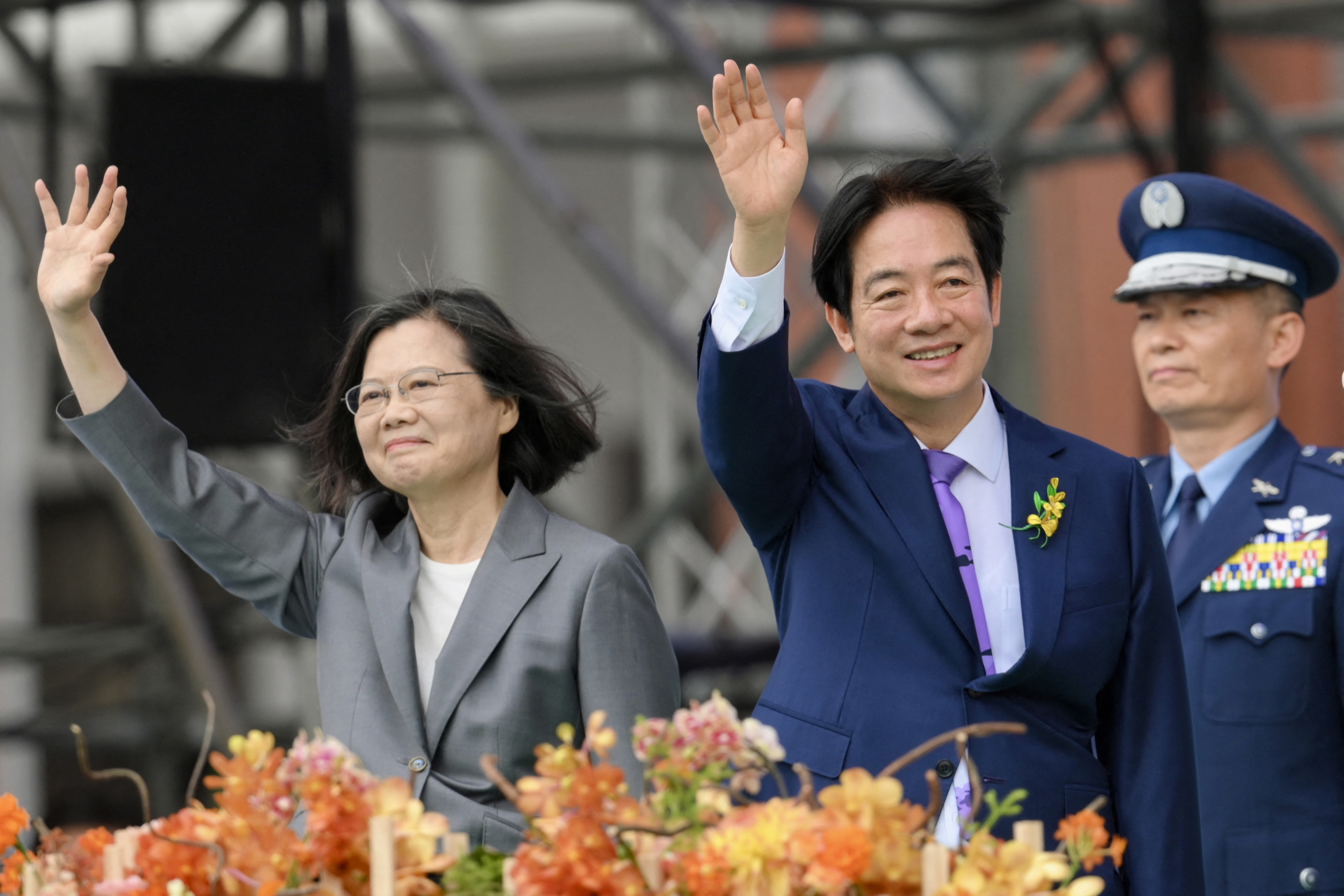 William Lai Ching-te smiles and waves after taking his oath of office. HIs predecessor Tsai Ing=wen is next to him. She is also waving and smiling.