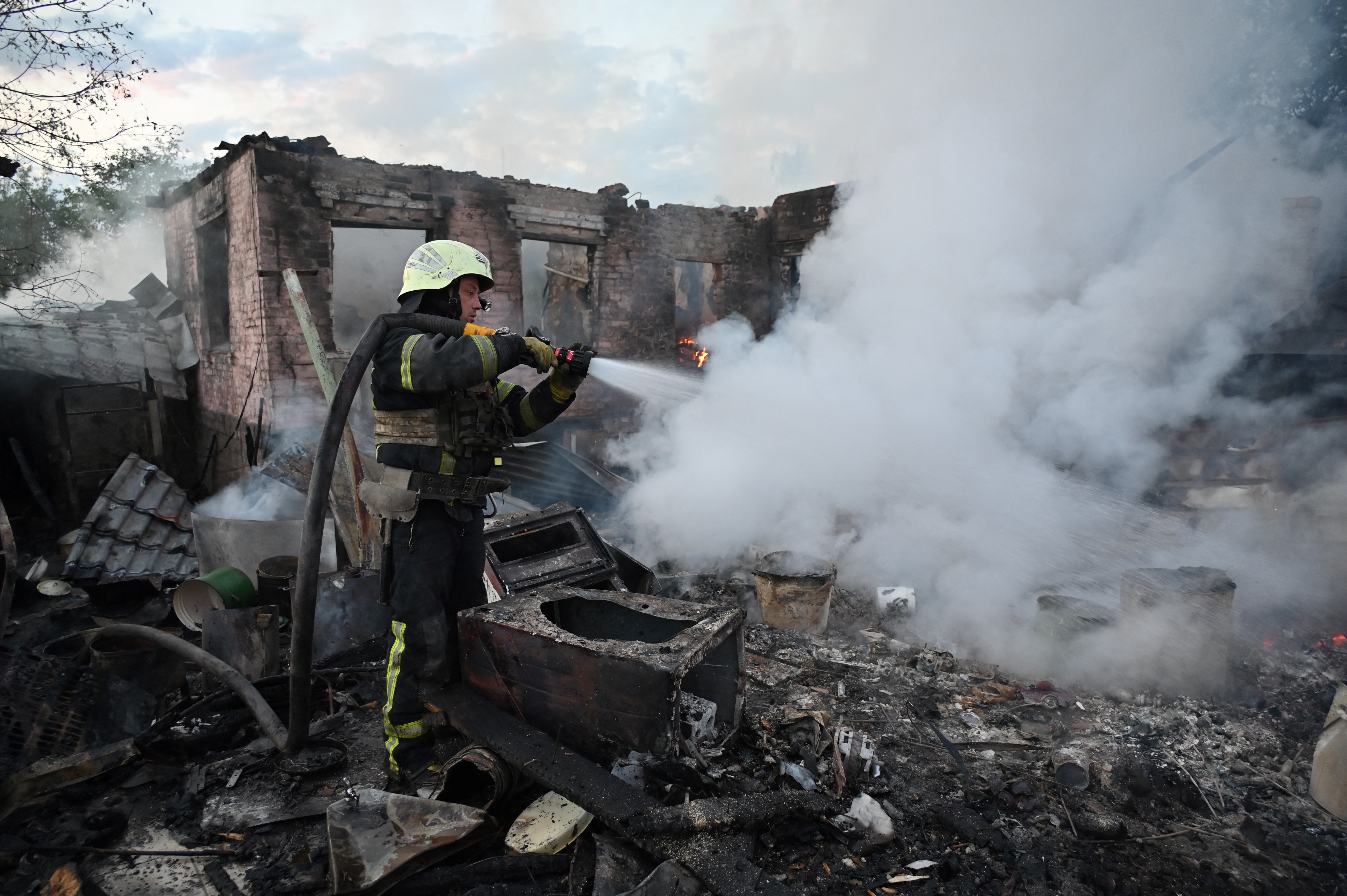 A firefighter directing water onto a fire at a private house caused by a Russian attack. Tne building is in ruins. Smoke is rising from the ashes
