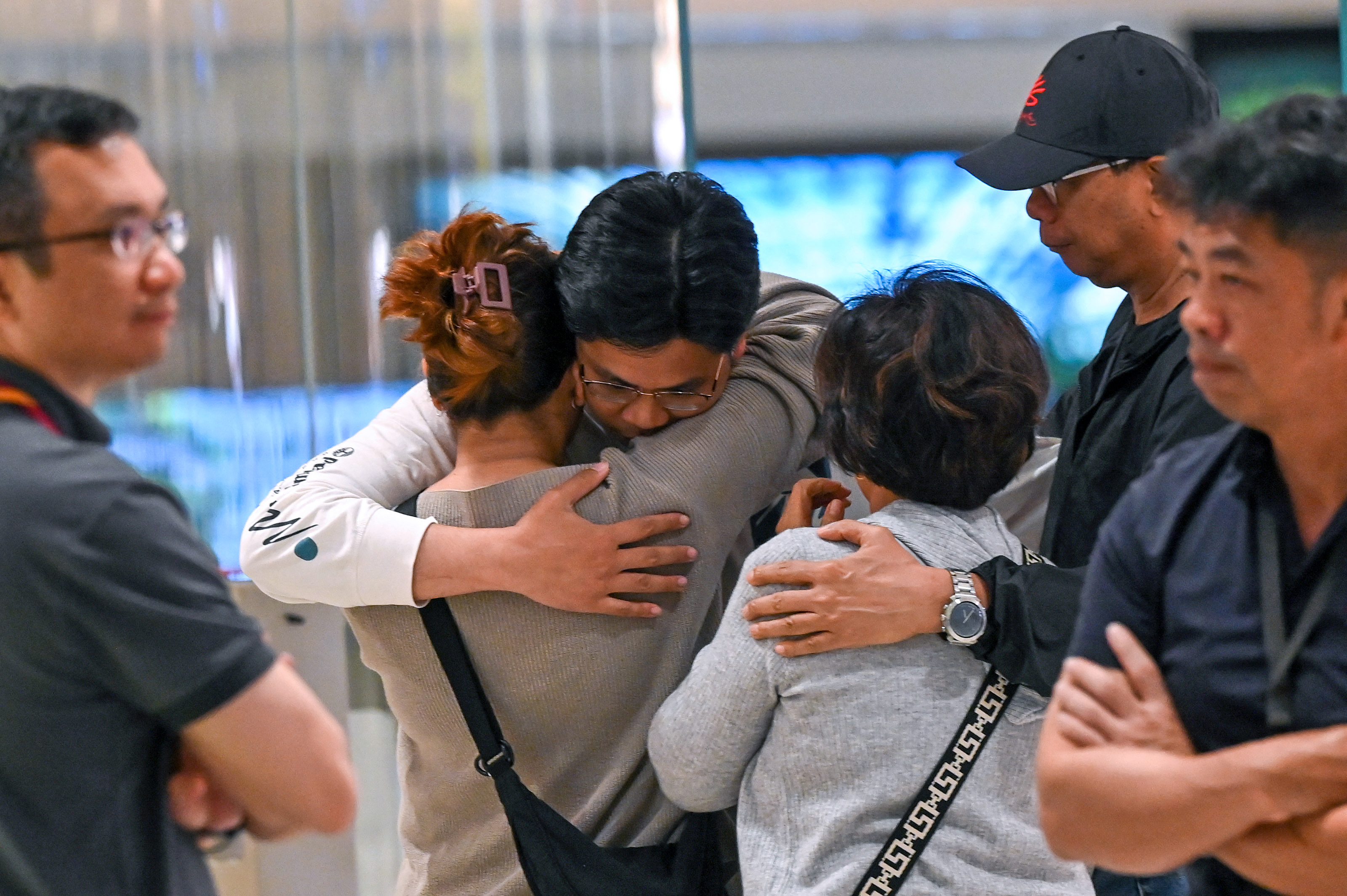 A man and a woman hug as family members look on after passengers from flight SQ321 arrived in Singapore