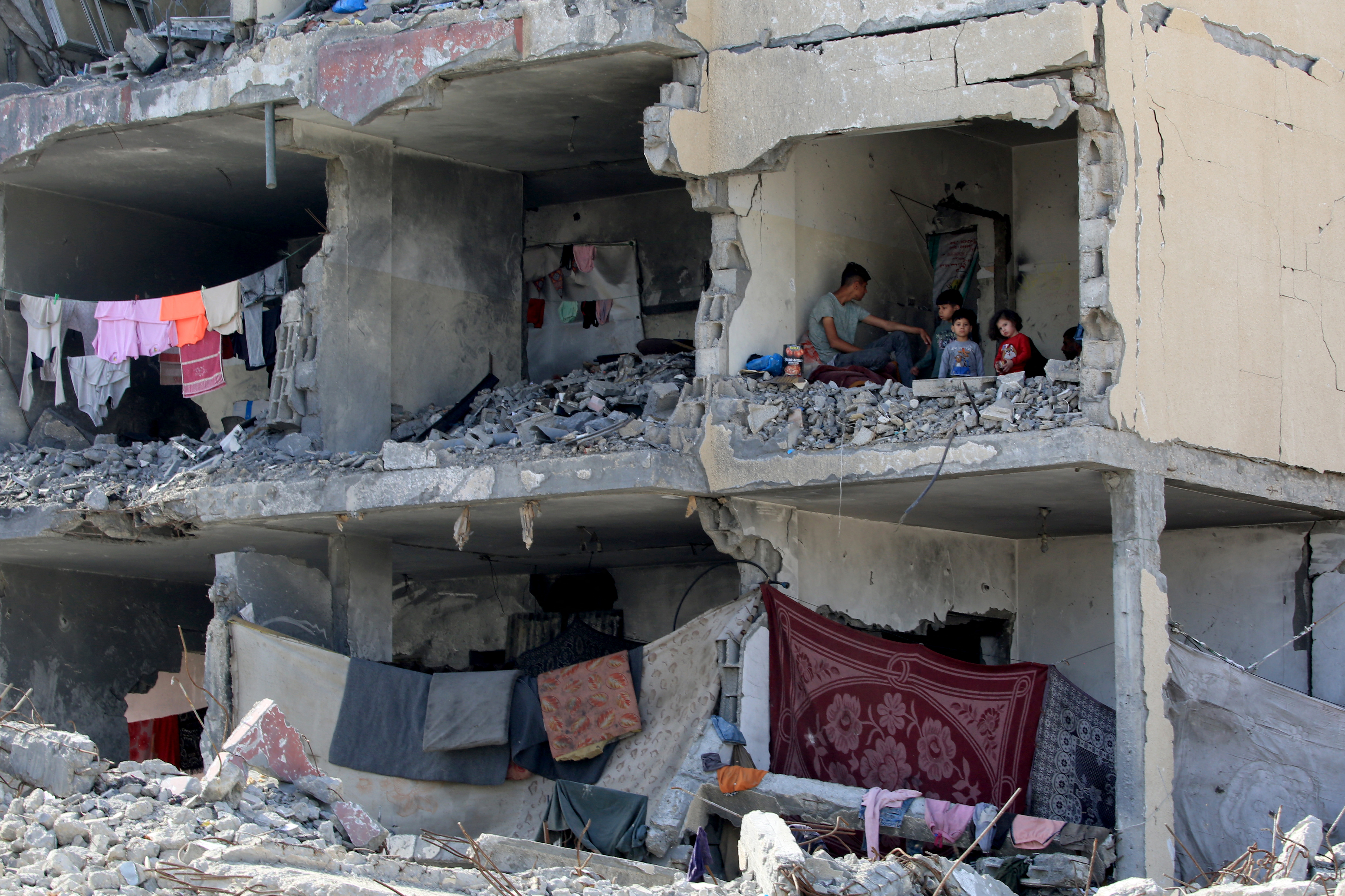 A Palestinian man and his children sit in a destroyed room following the targeting or a residential building by an Israeli airstrike in Rafah in the southern Gaza Strip on May 22