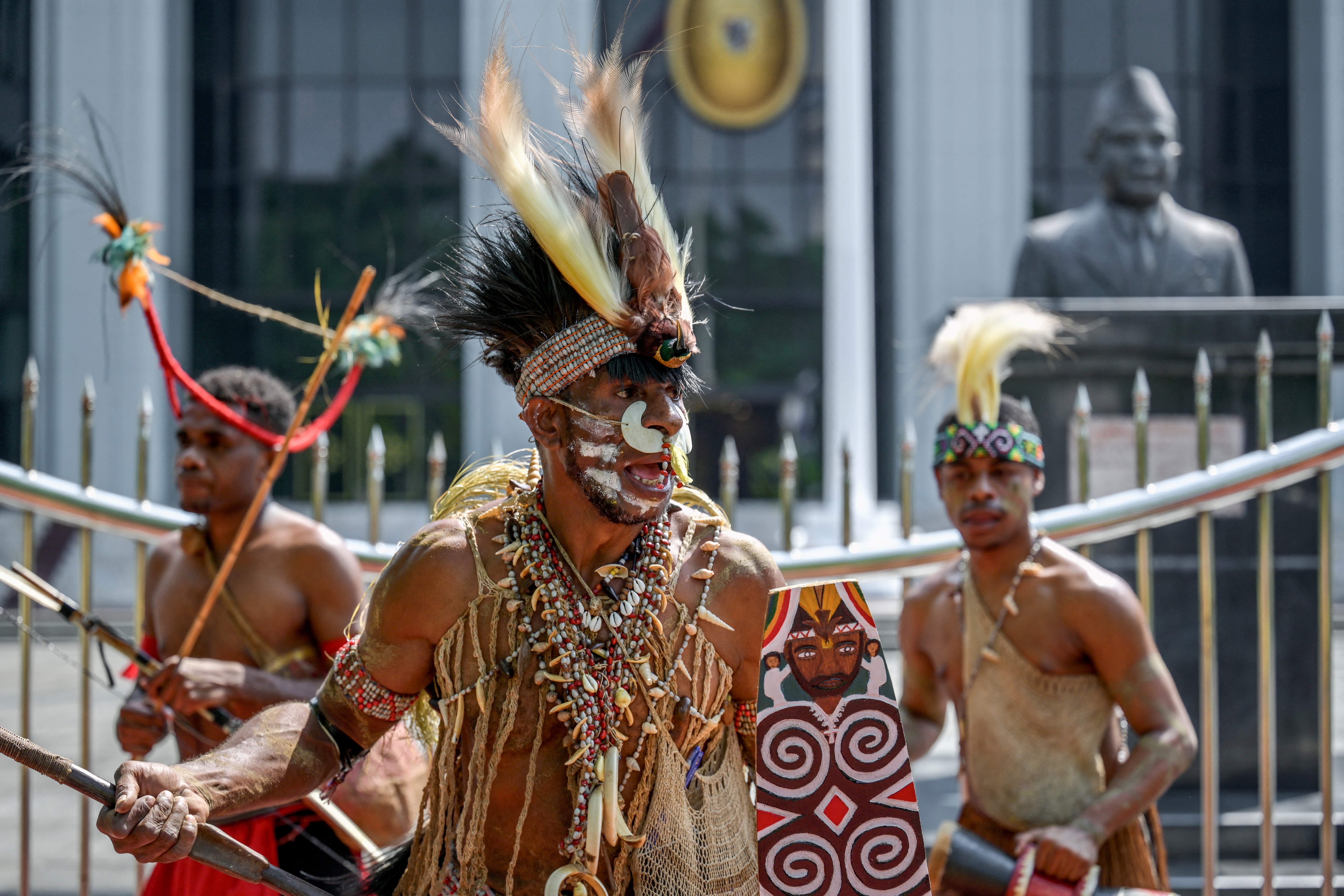Representatives of the Awyu and Moi indigenous tribes dance in front of the court. They are in traditional clothing and wearing feather headdresses.