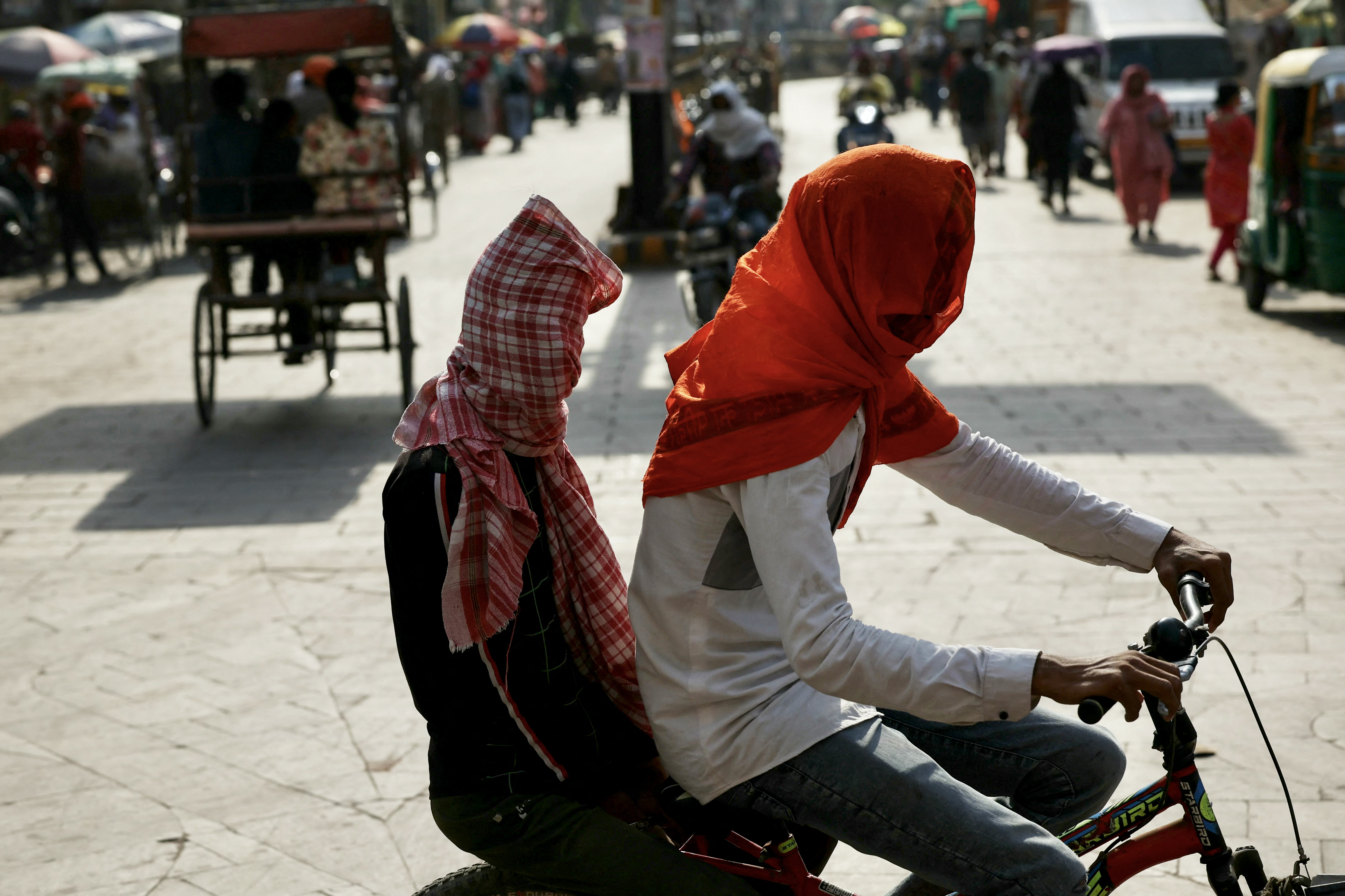 Boys riding a bicycle cover their faces in Varanasi amid heatwave