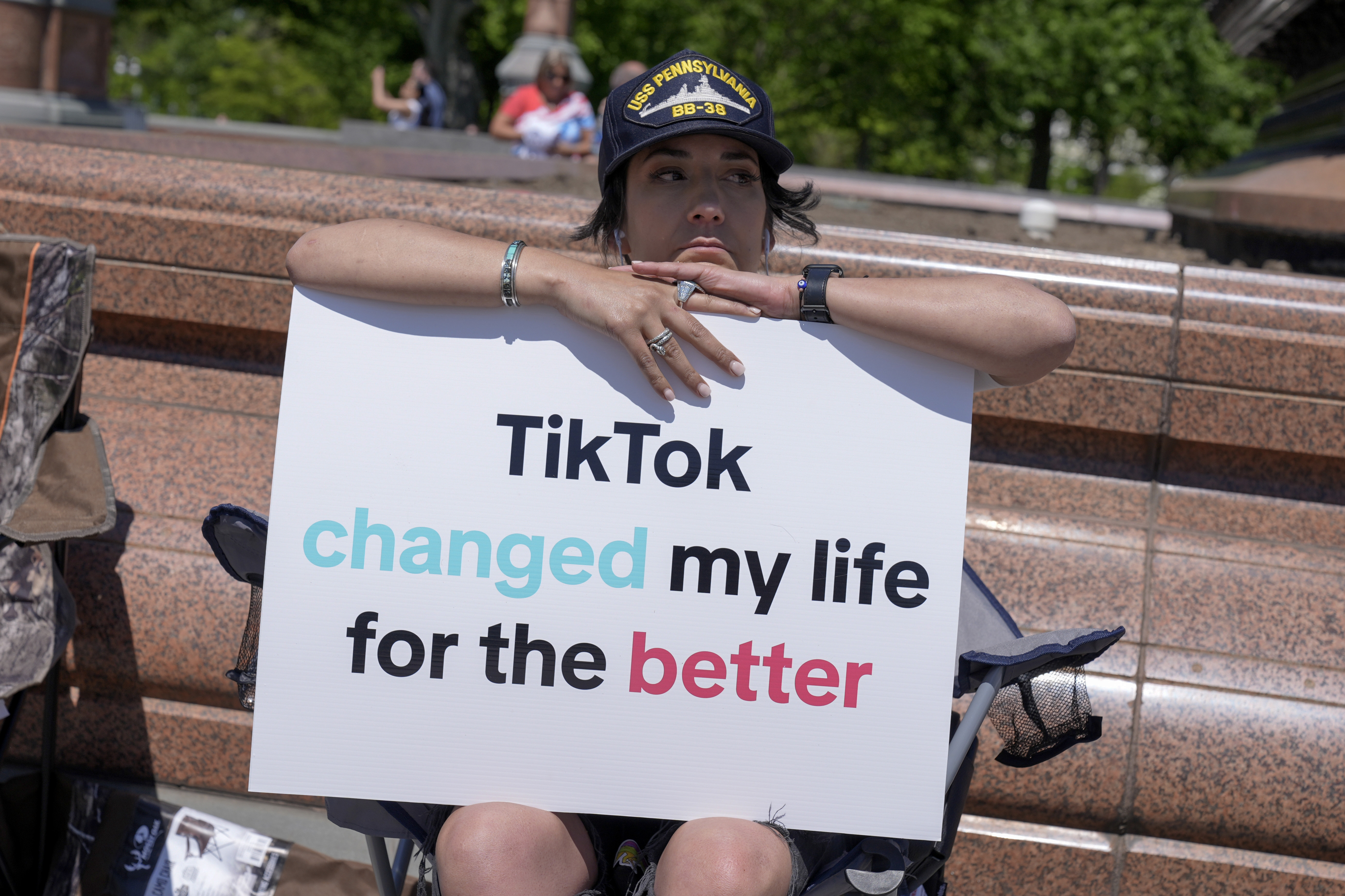 A young person poses with her arms atop a sign that reads, "TikTok changed my life for the better."