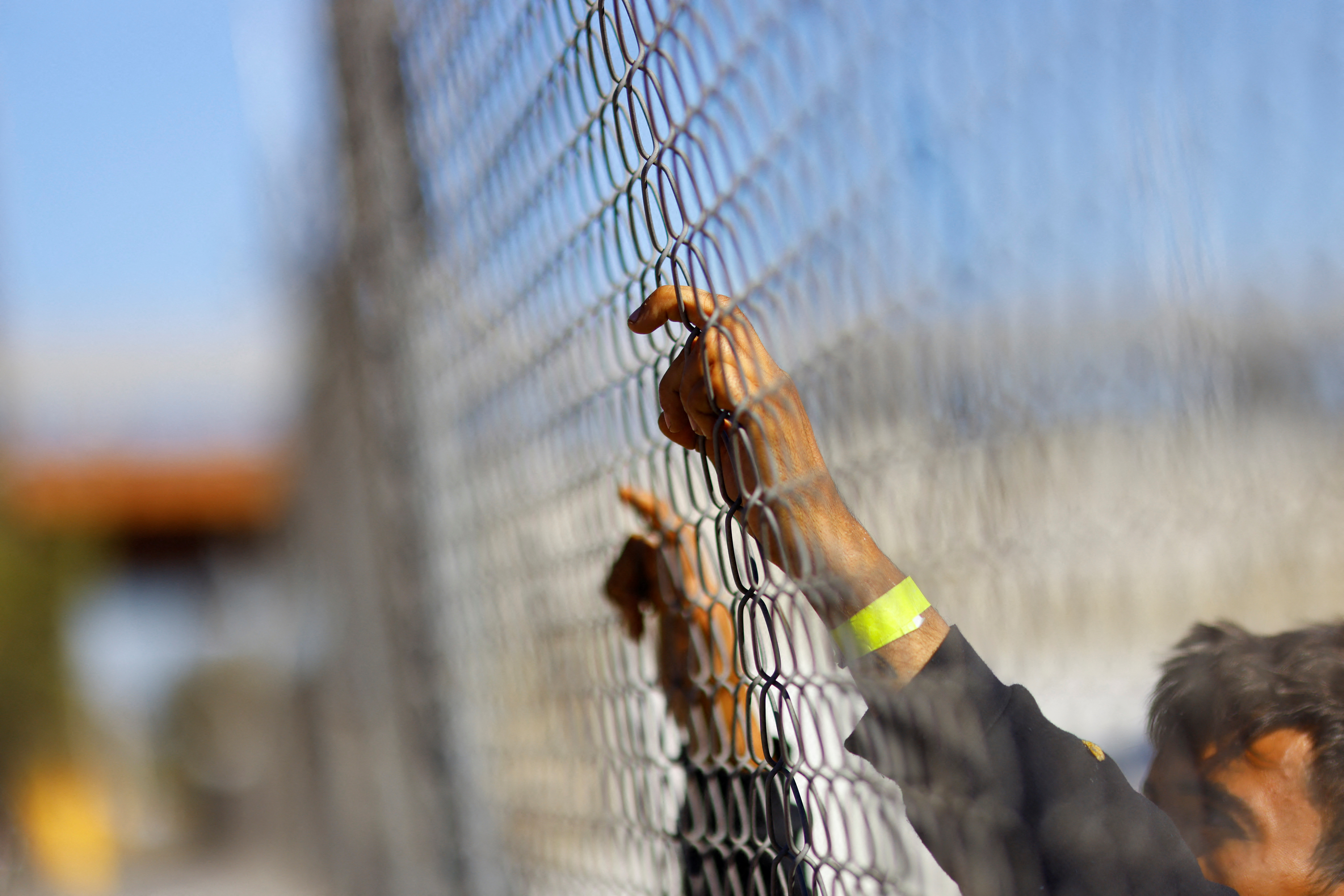 An asylum seeker expelled from the US holds onto a fence at the border with Mexico