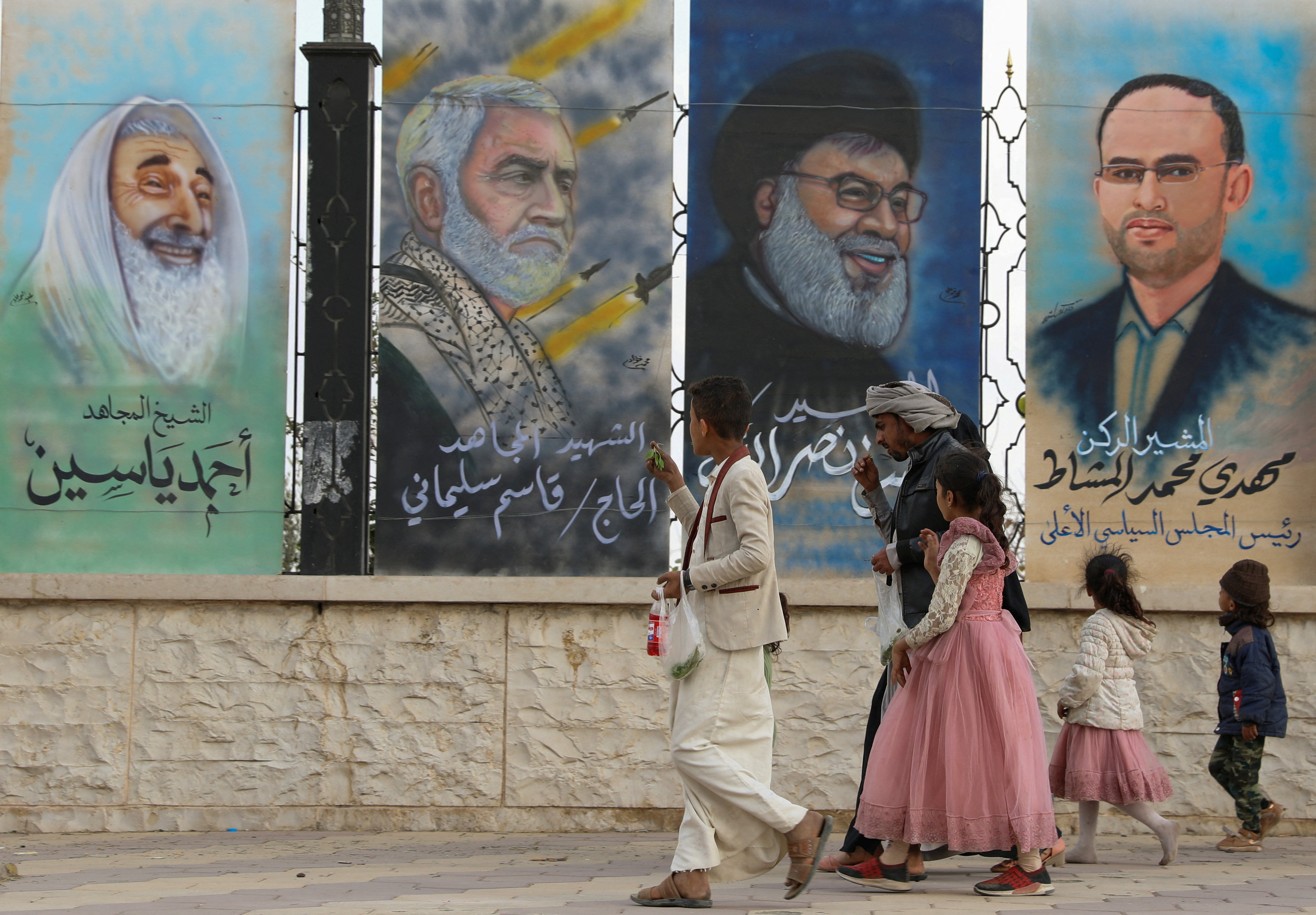 People walk past posters of former Hamas leader Ahmad Yassin, former chief of Iranian Quds Force Qassem Suleimani, Lebanon's Hezbollah chief Sayyed Hassan Nasrallah and Houthi leader Mahdi al-Mashat at the Sabeen Square in Sanaa, Yemen