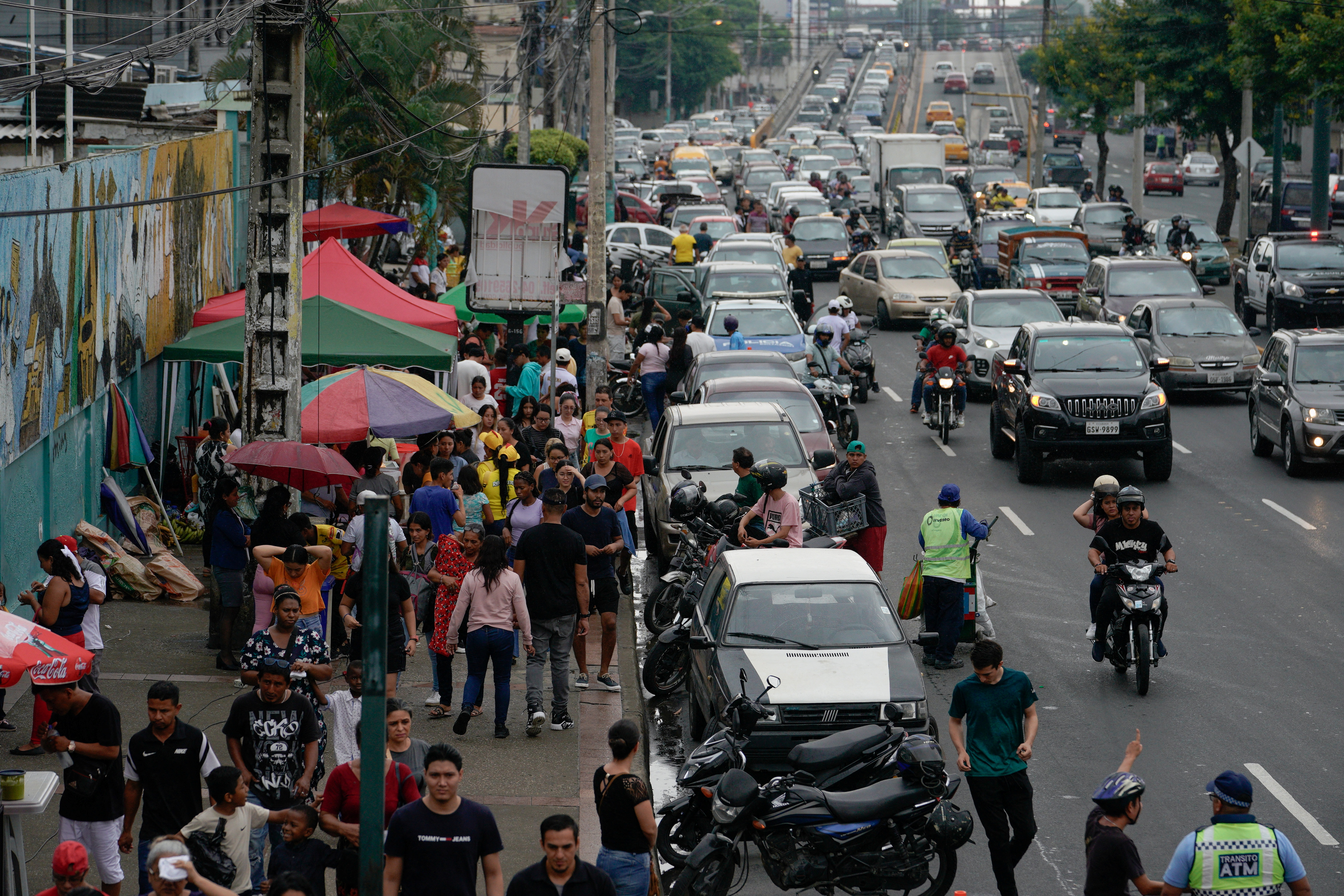 A street scene in Guayaquil, seen from above: cars and pedestrians navigating a busy street, moving past vendors with umbrellas.