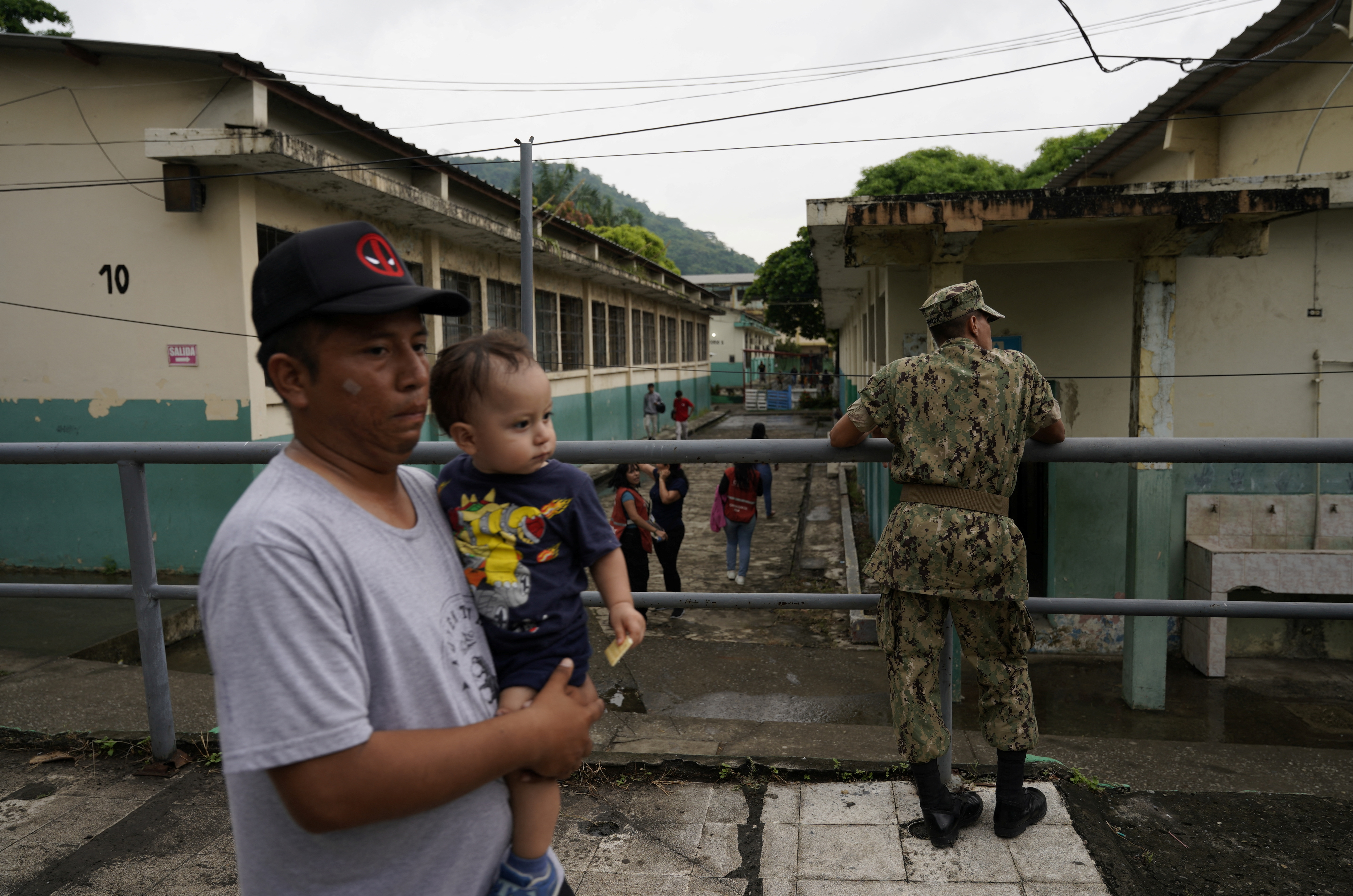 A man with a baby in his arms walks past a soldier on an elevated walkway.