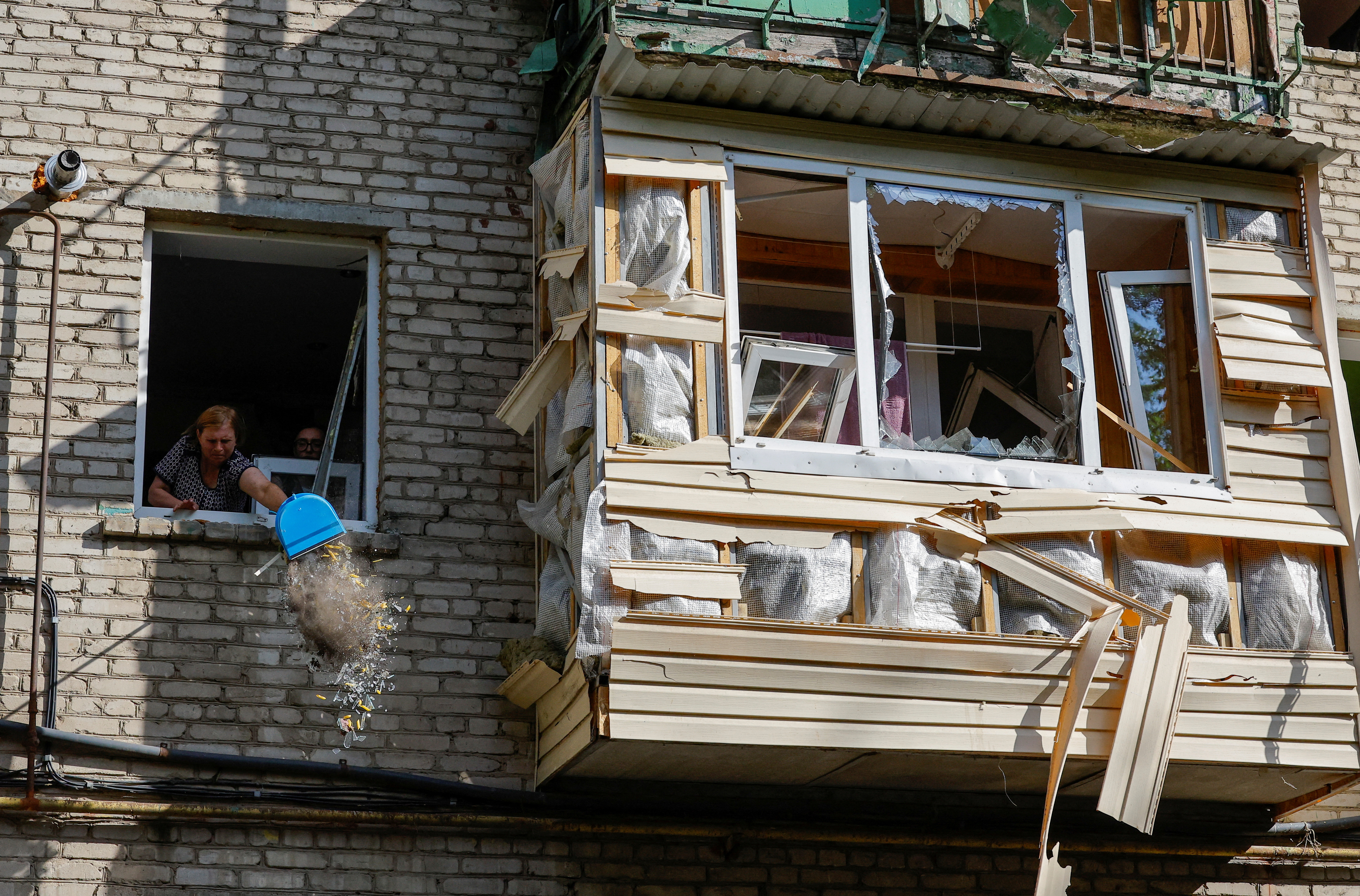 A woman cleans debris from an apartment in a multi-storey residential building damaged in recent shelling by U.S.-supplied ATACMS missiles