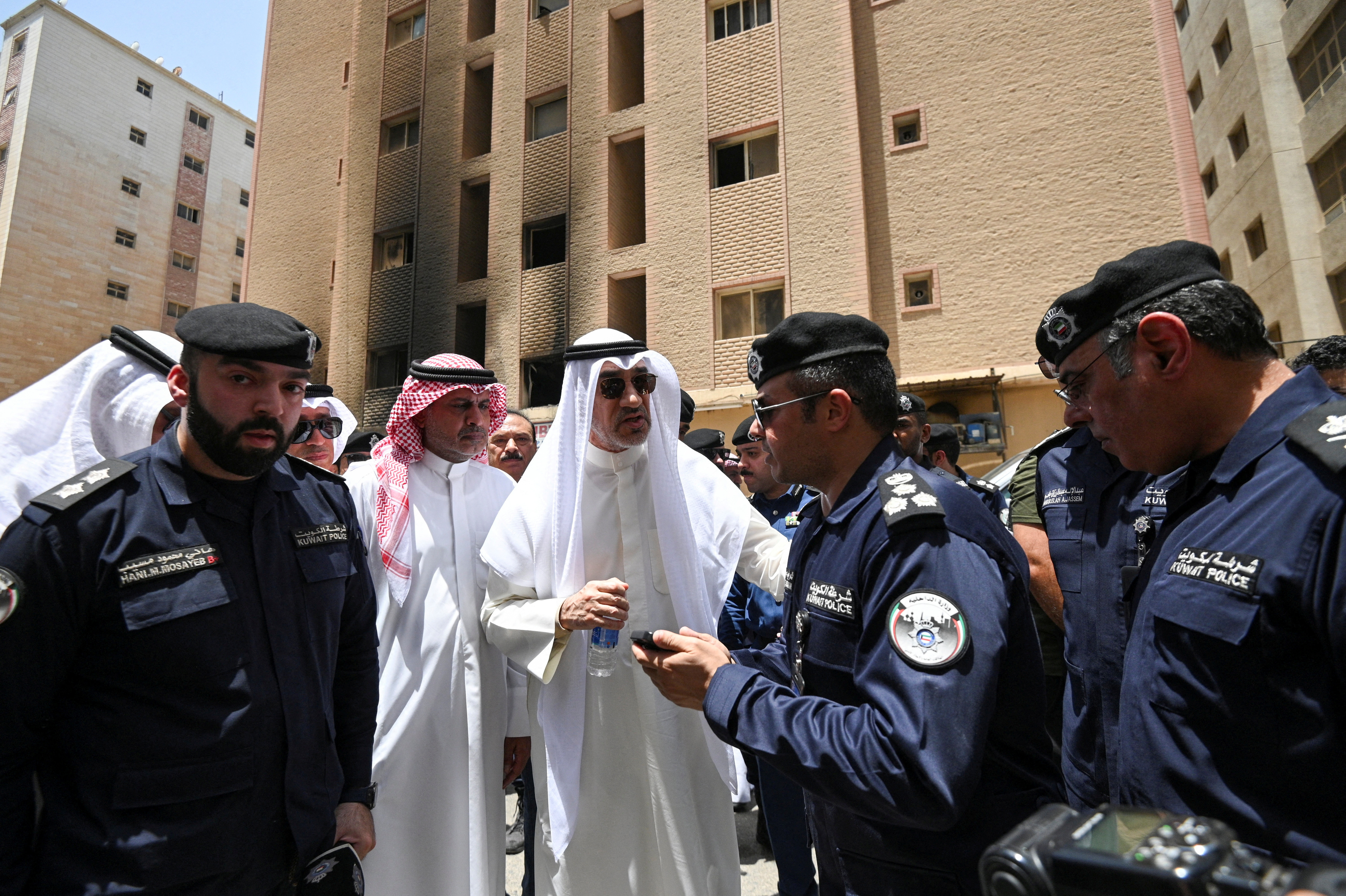 Kuwait's Deputy Prime Minister and Minister of Defense and acting Interior Minister, Fahad Yusuf Al-Sabah speaks with police officers in front of a burnt building