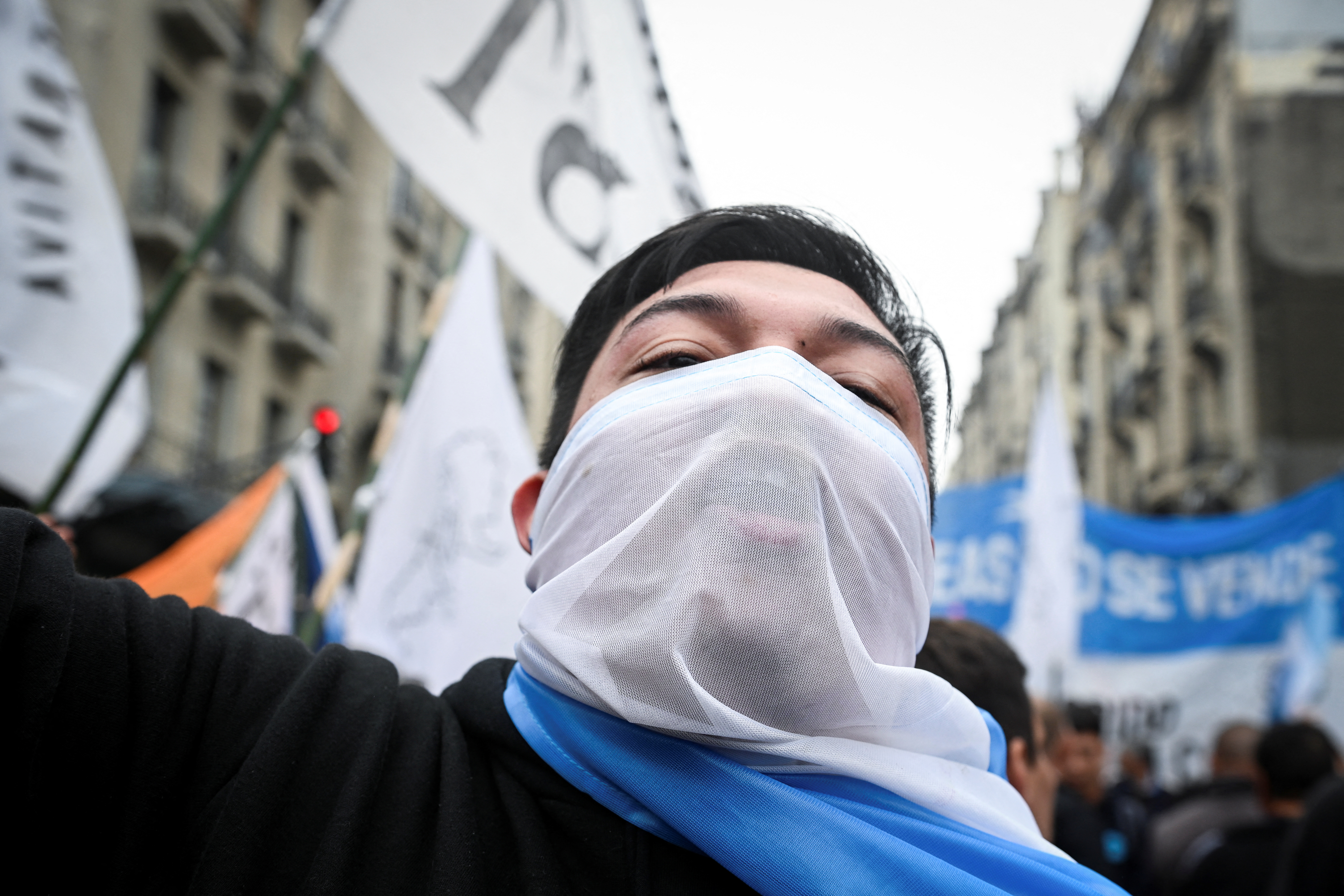 A close-up of a protester wearing a white cloth over his lower face as he marches through the streets of Buenos Aires.