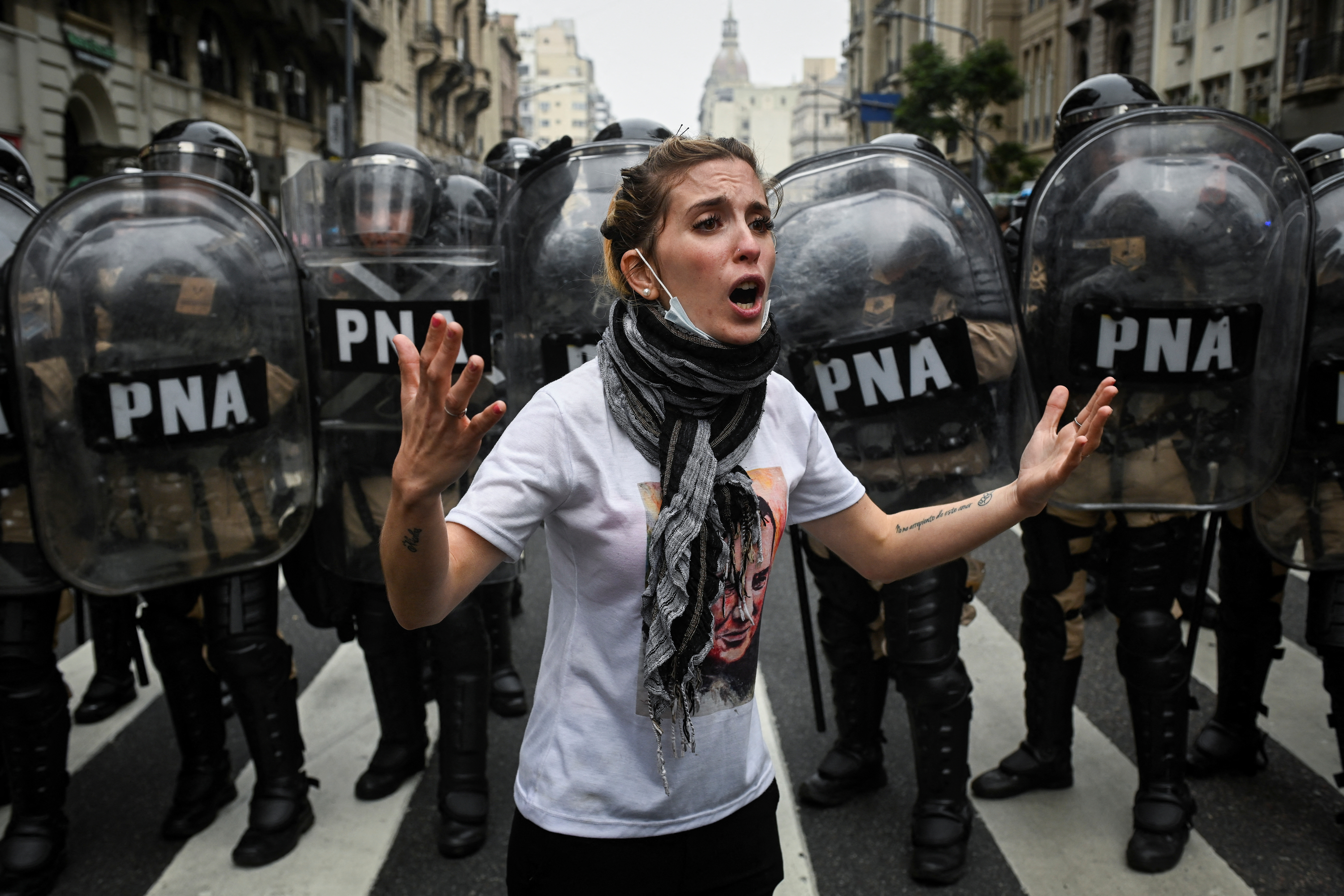 A woman shouts, with her arms outspread, as a line of riot police advance behind her in Buenos Aires's streets.