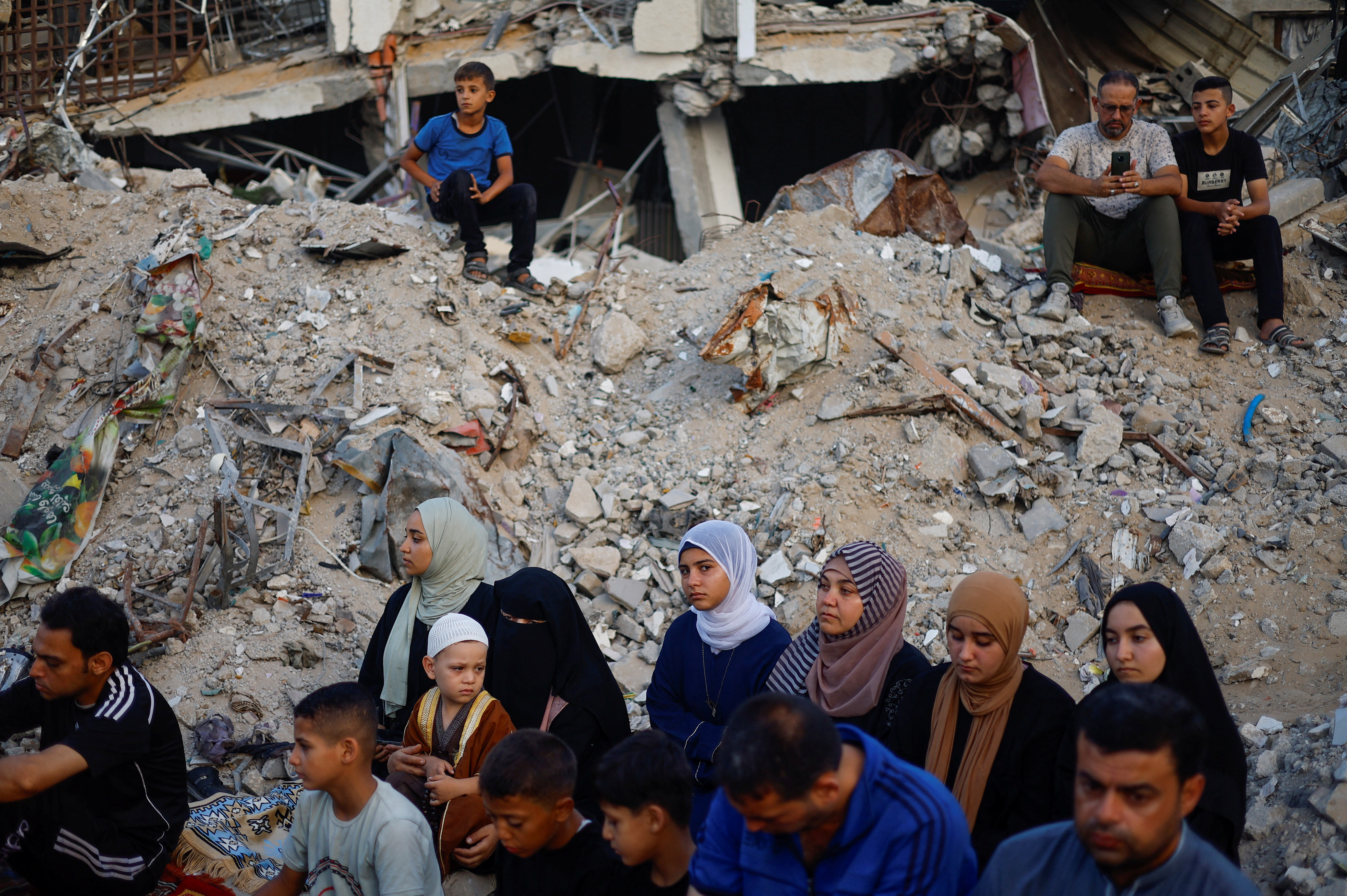 People sit in among the rubble