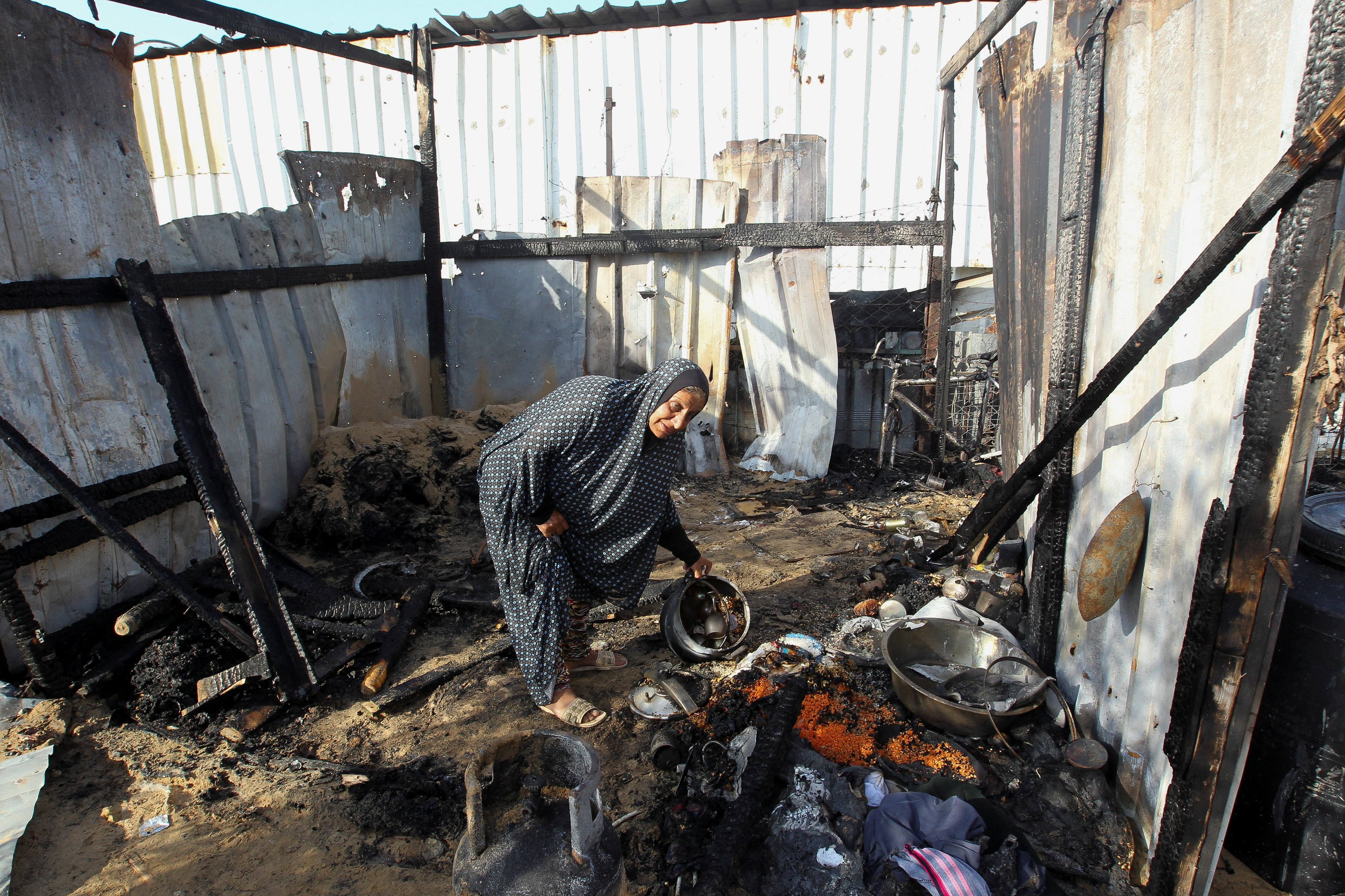 A Palestinian woman inspects a shelter among burnt debris after an Israeli strike on an area designated for displaced people