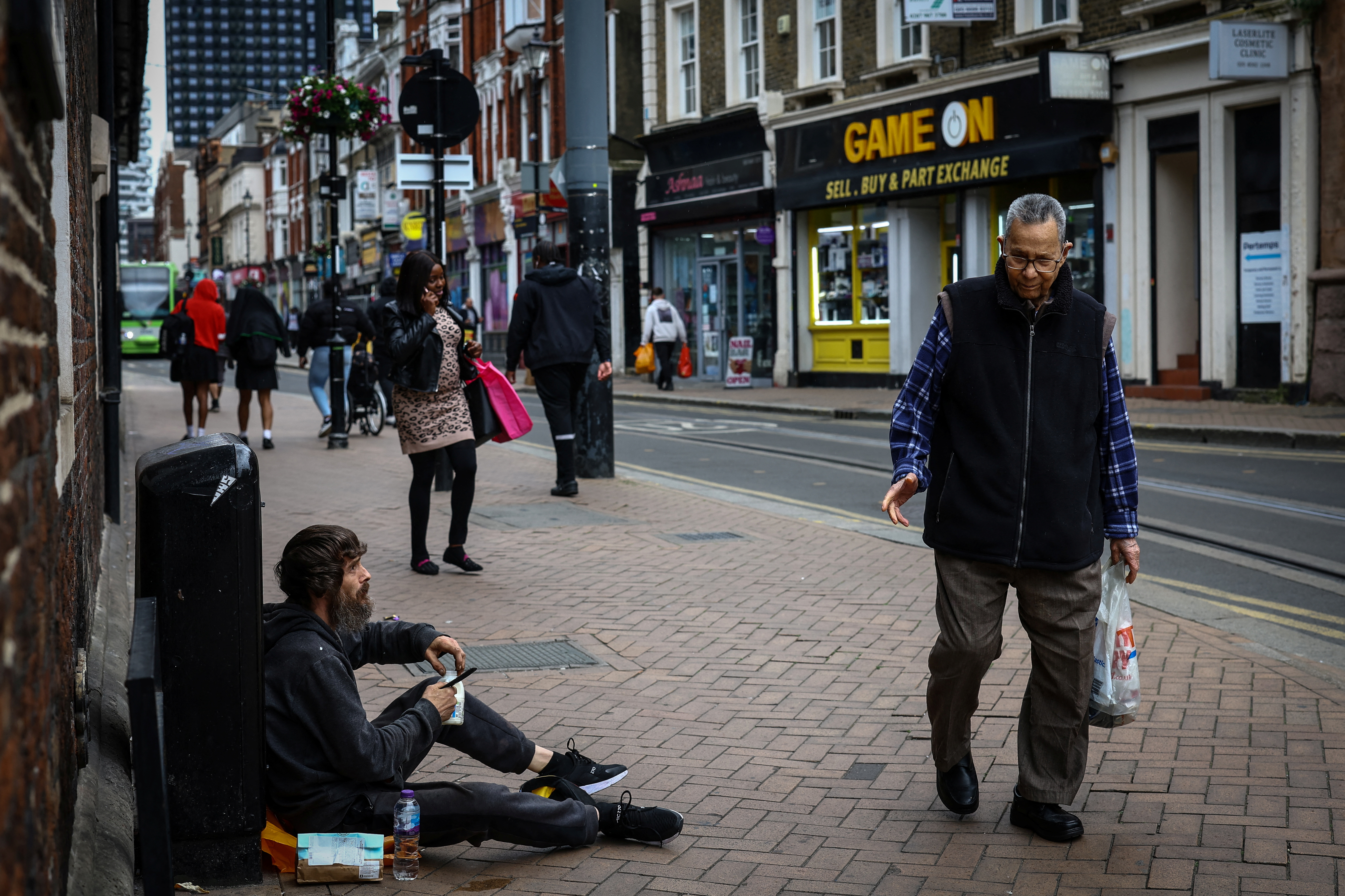 People walk past a man who is homeless on a high street in Croydon, south London, Britain, June 13