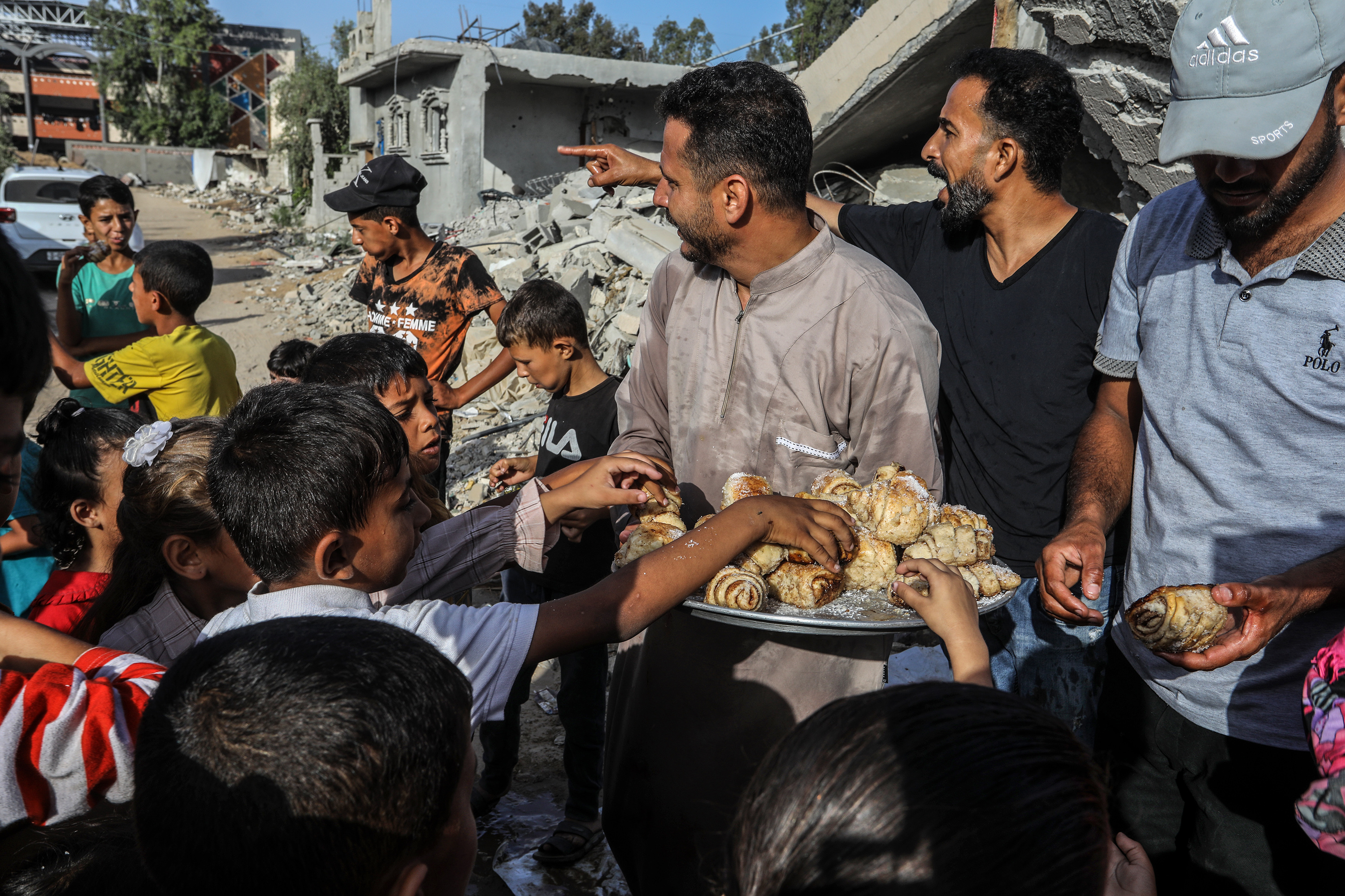 A Palestinian man distributes sweet buns within Eid al-Adha among the rubble of buildings destroyed by Israeli attacks in Khan Yunis, Gaza on June 16
