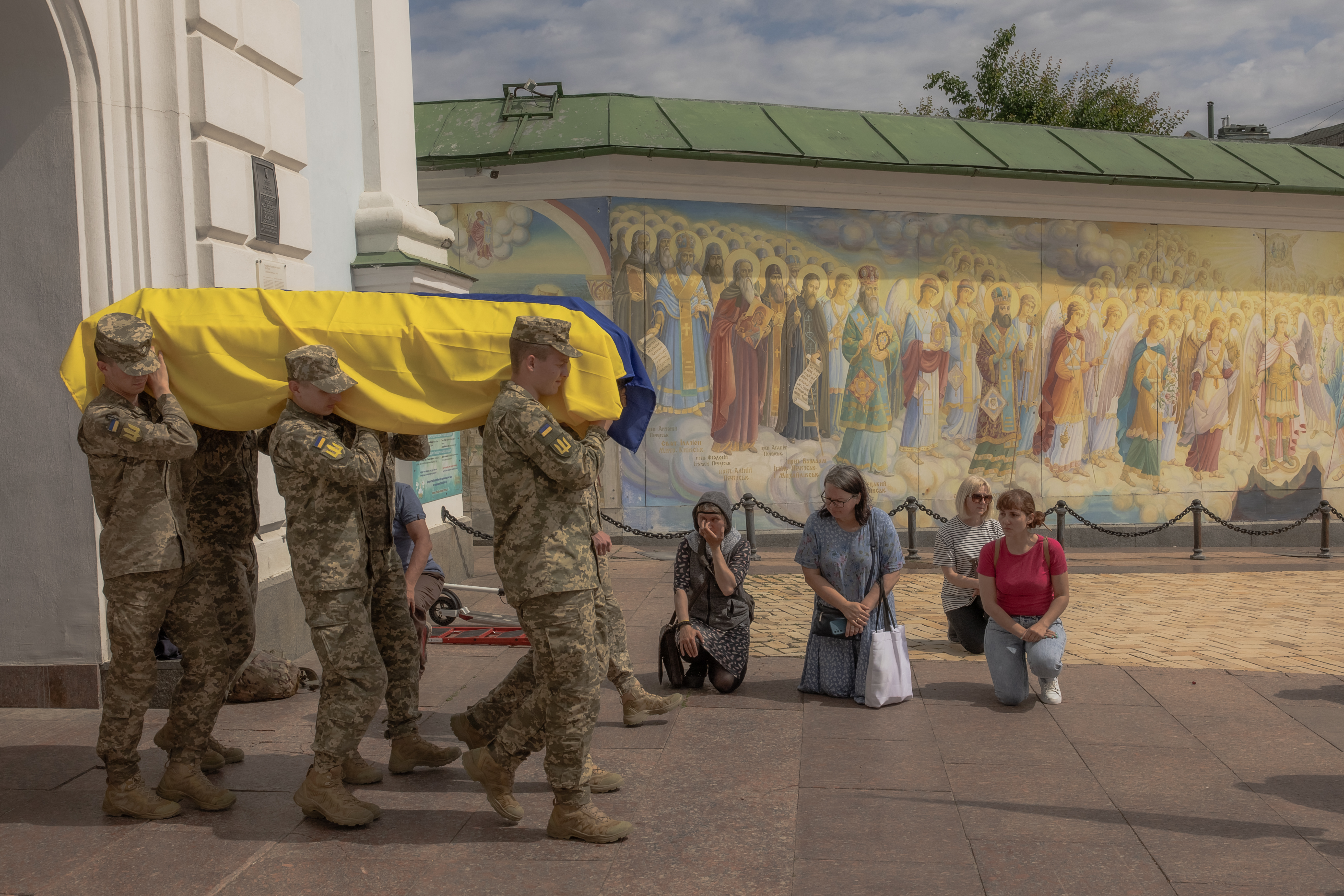 People kneel as Ukrainian soldiers carry the coffin of Ukrainian serviceman Ruslan Troianchuk, callsigned "Friend", who was killed in the Donetsk region, during his funeral service outside Saint Michael's Golden-Domed Monastery in Kyiv on May 28