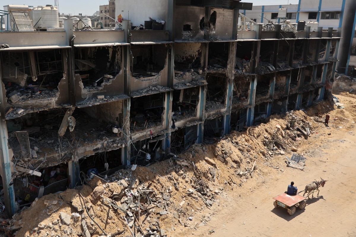 A Palestinian man rides a donkey-pulled cart past a damaged UN-run school in the Jabalia