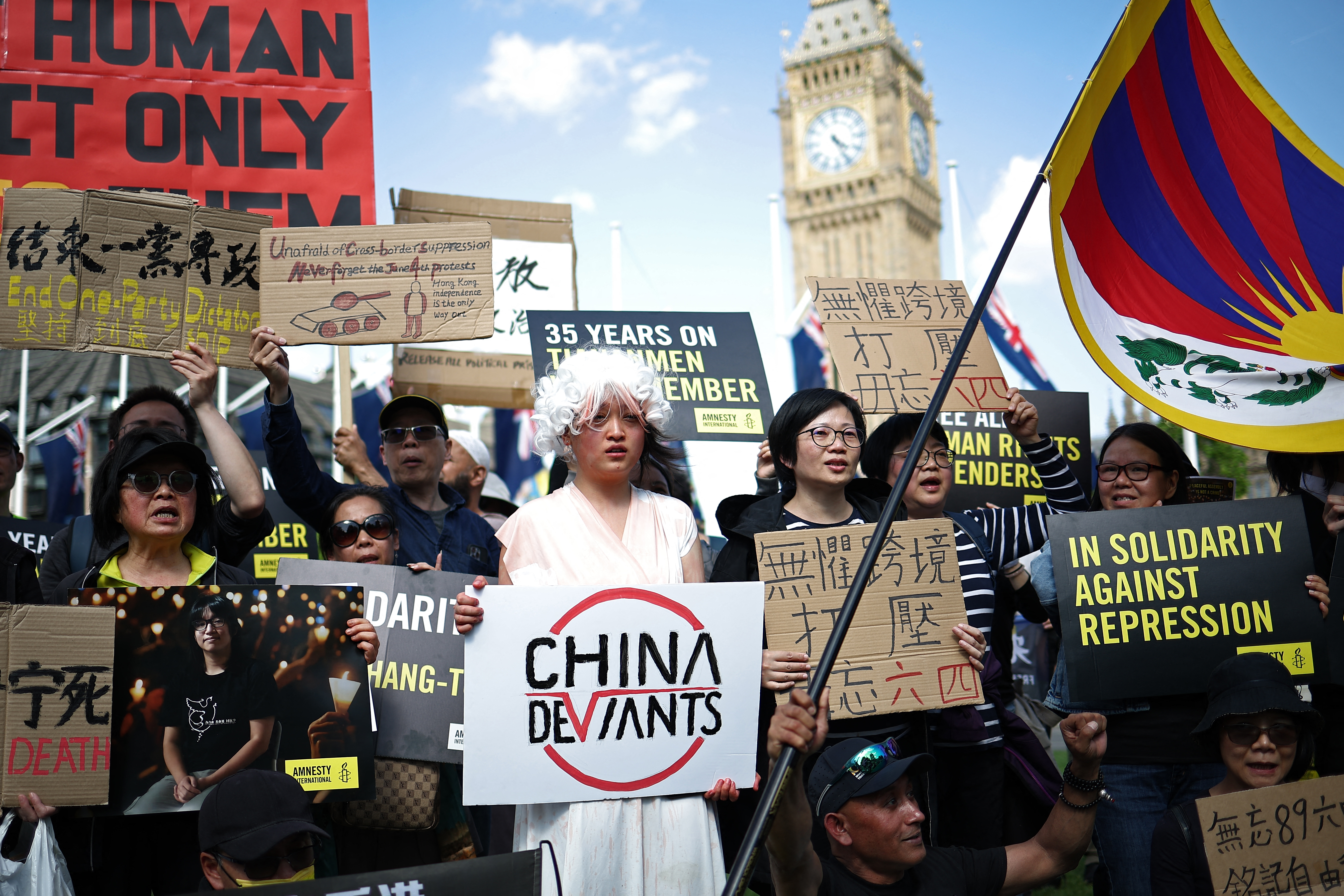 Protesters gather in London to remember Tiananmen. They have flags and placards. One is waving a Tibetan flag.