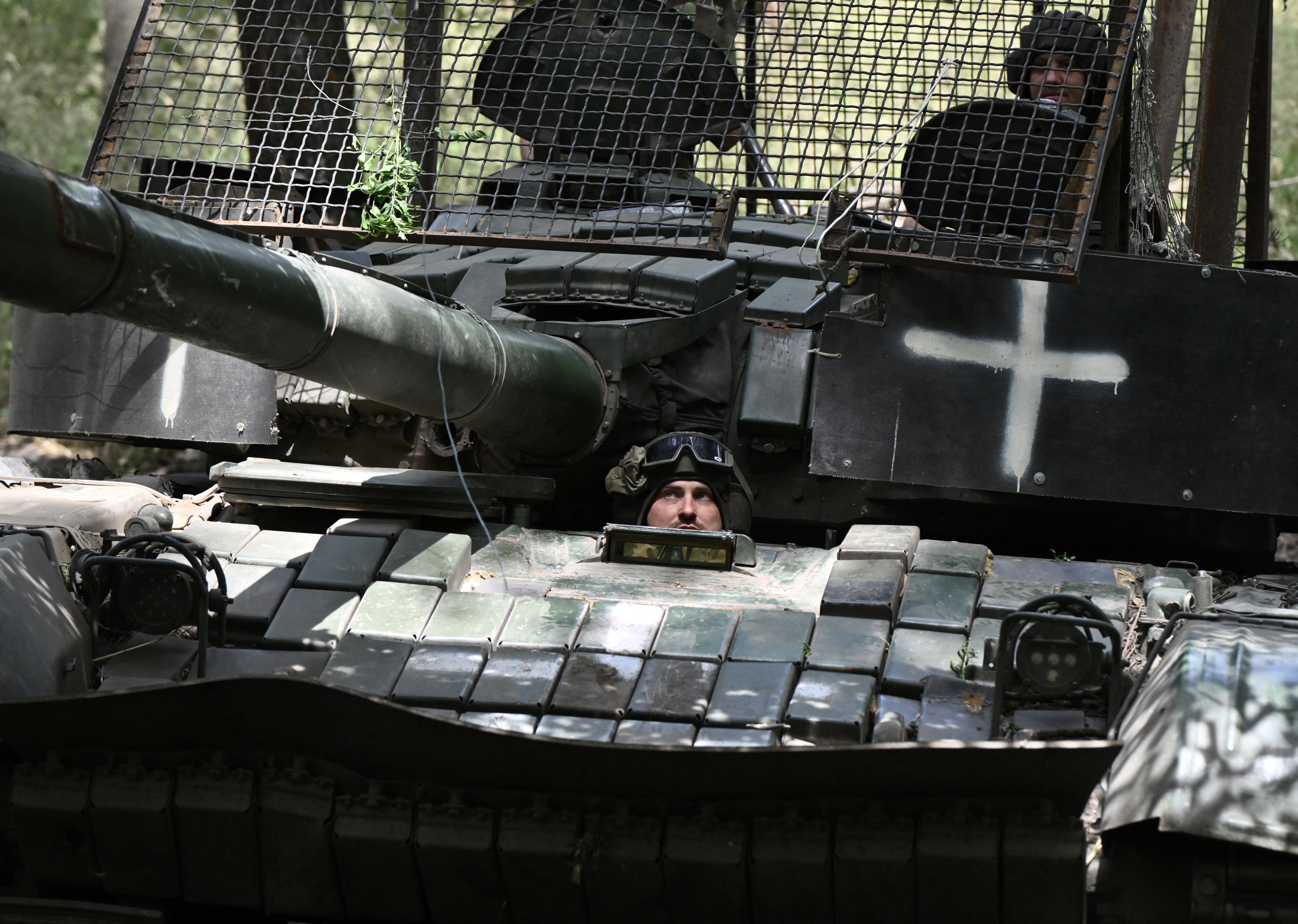 A Ukrainian soldier looking out from a tank beneath the gun. A white cross is painted on the vehicle.