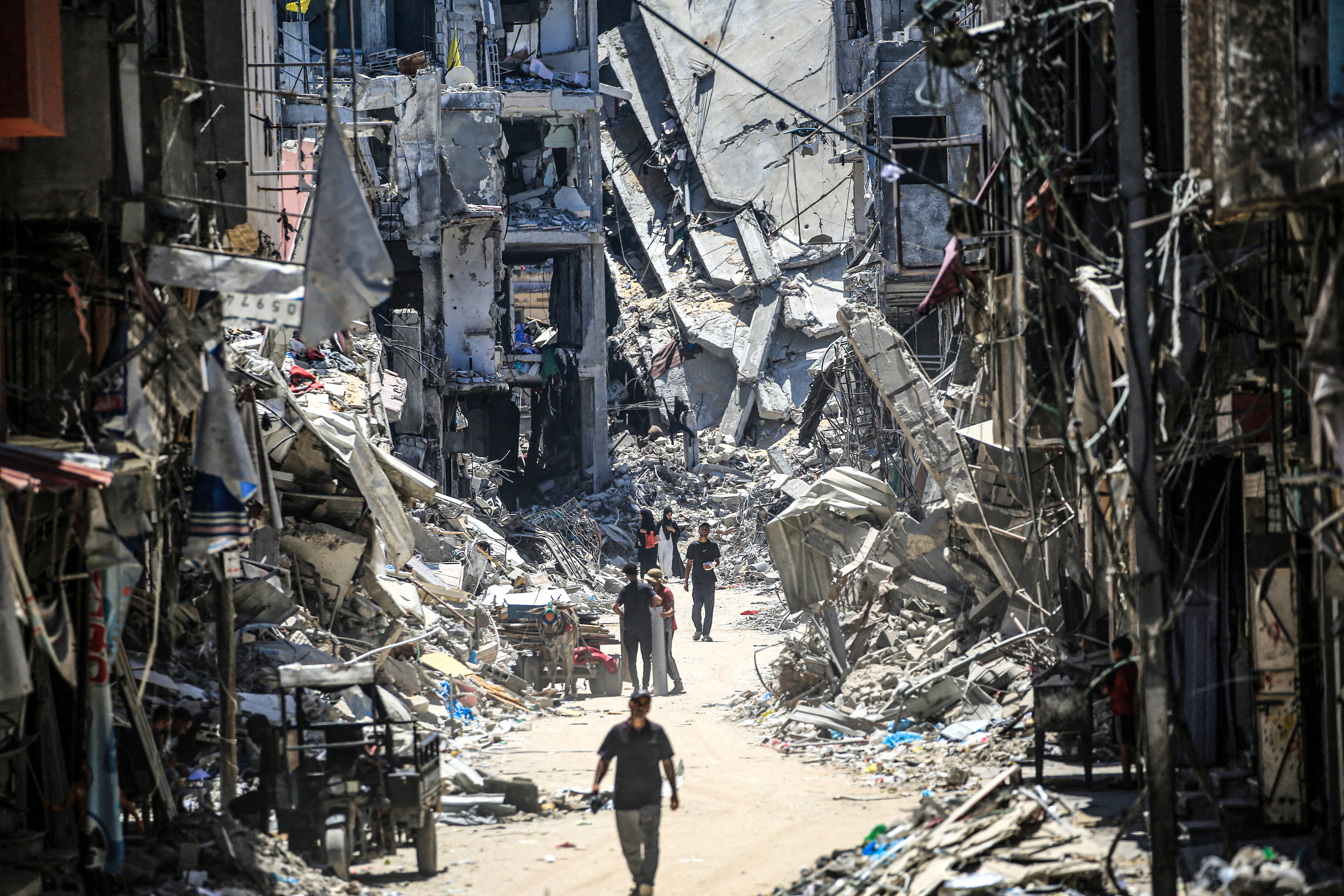 Palestinian men walk along a narrow street past destroyed buildings in Khan Yunis