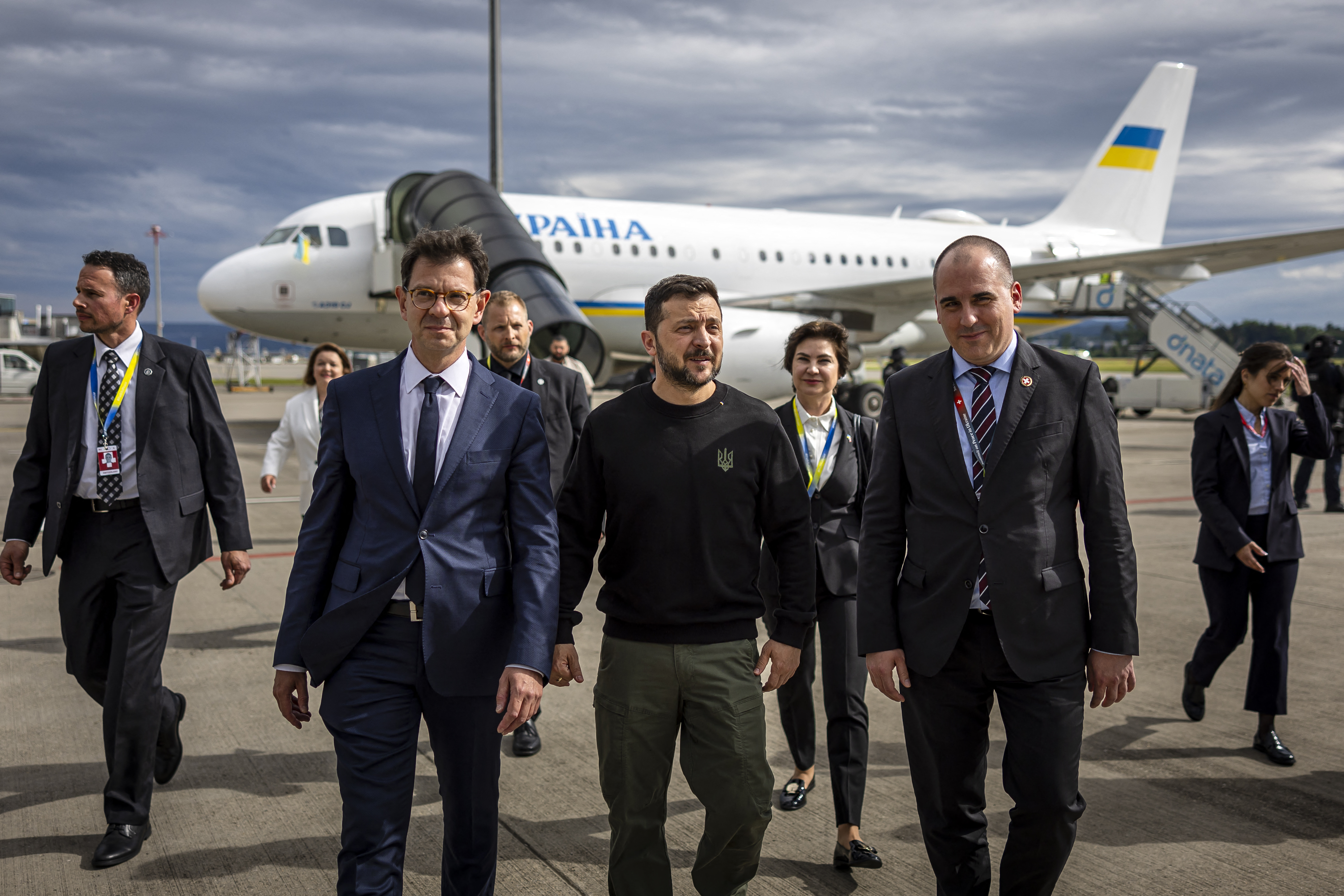 Ukraine's President Volodymyr Zelensky (C) is welcomed by Switzerland's Ambassador to Ukraine Felix Baumann (L) and Deputy Head of Swiss Protocol Manuel Irman (R) as he arrives at the Zurich airport on June 14, 2024, ahead of the Ukraine Peace Summit in Switzerland. World leaders from countries around the world will gather in the luxury Burgenstock resort, central Switzerland this weekend to try to work out a way towards a peace process for Ukraine -- albeit without Russia. (Photo by MICHAEL BUHOLZER / POOL / AFP)