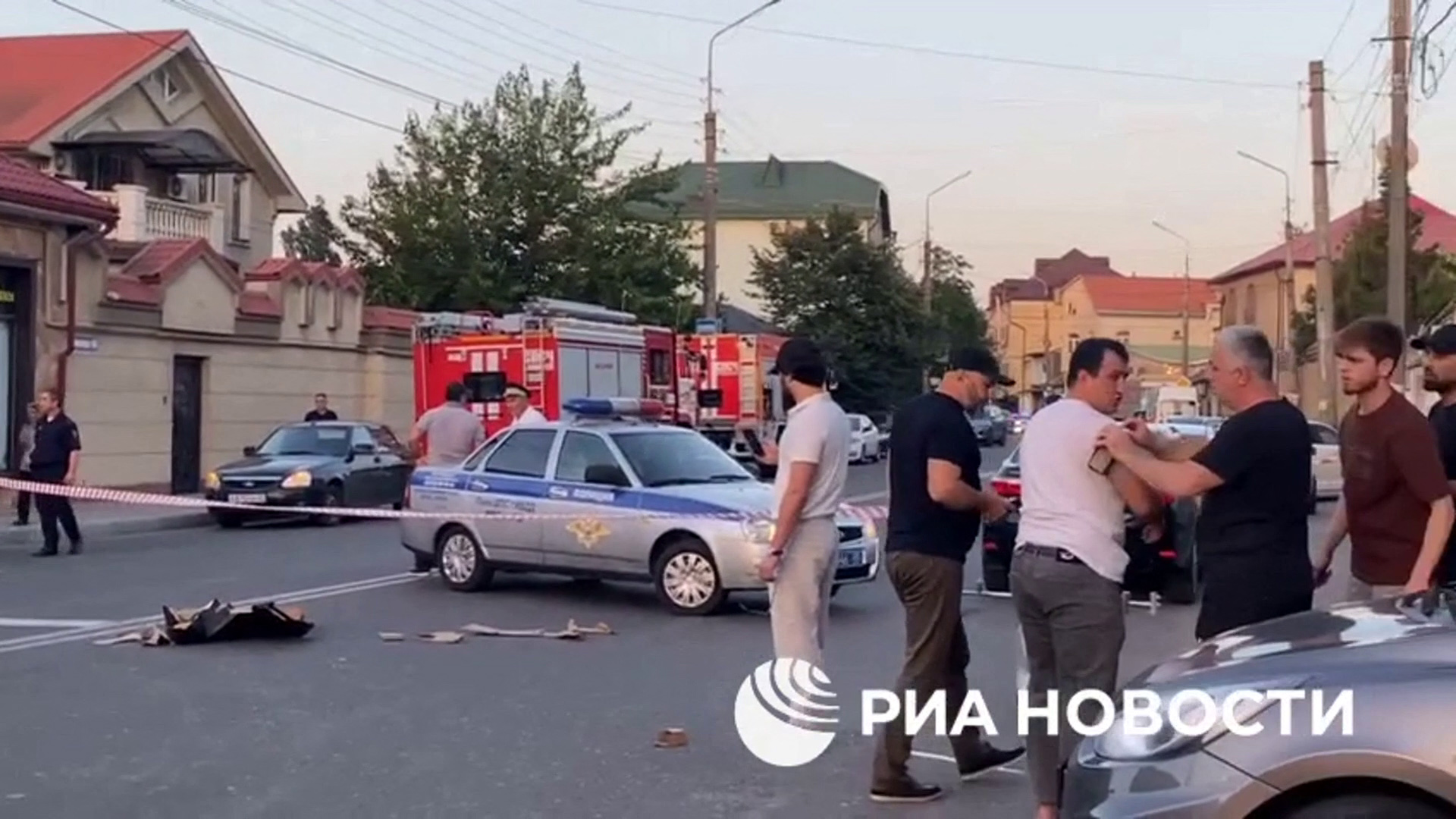 People gathered at an area sealed off by police in Dagestan. There are police cars in the road. The people look worried.