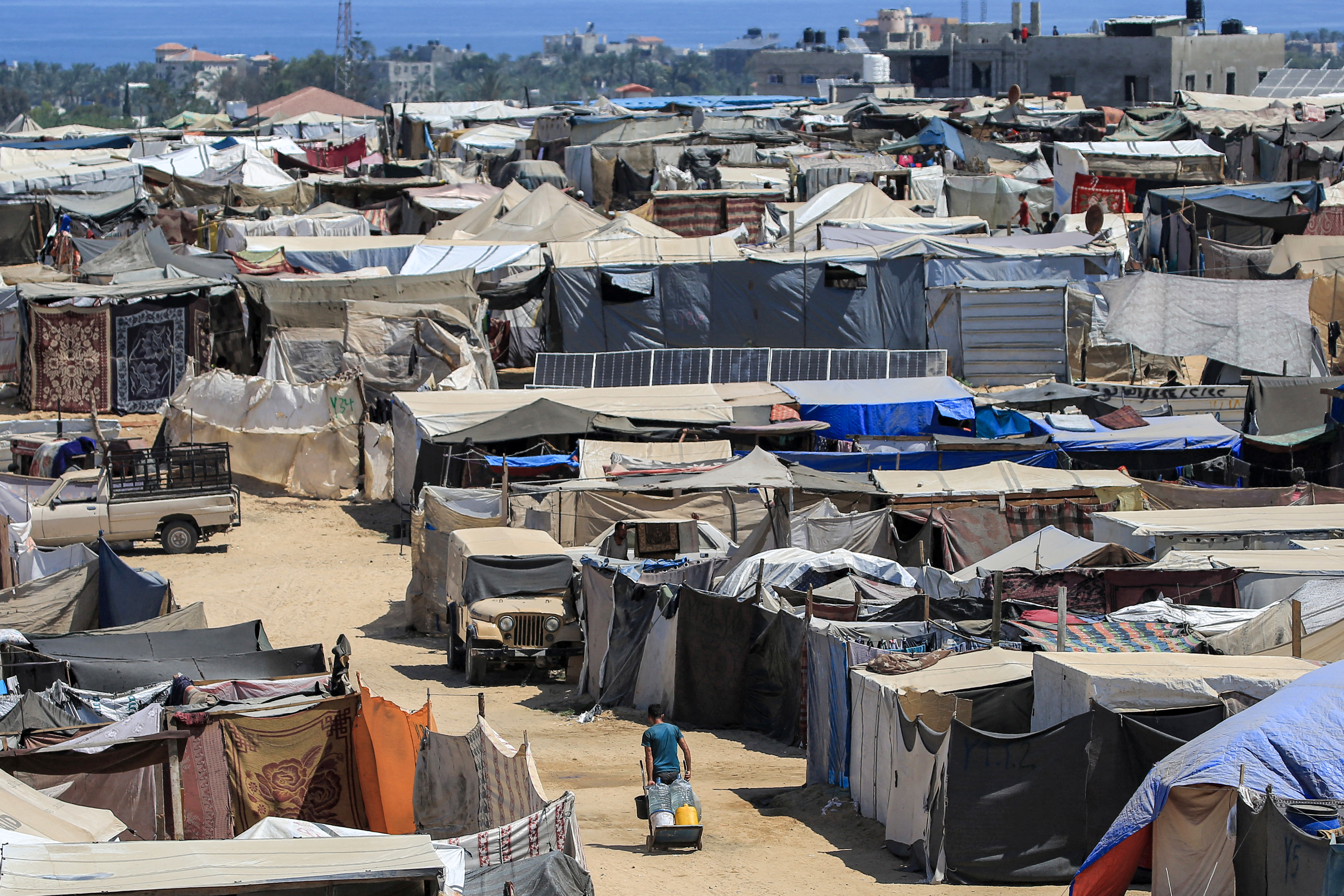 A man pulls a cart loaded with water containers after filling up from a water truck as he walks along an alley between tents sheltering displaced Palestinians in Rafah in the southern Gaza Strip