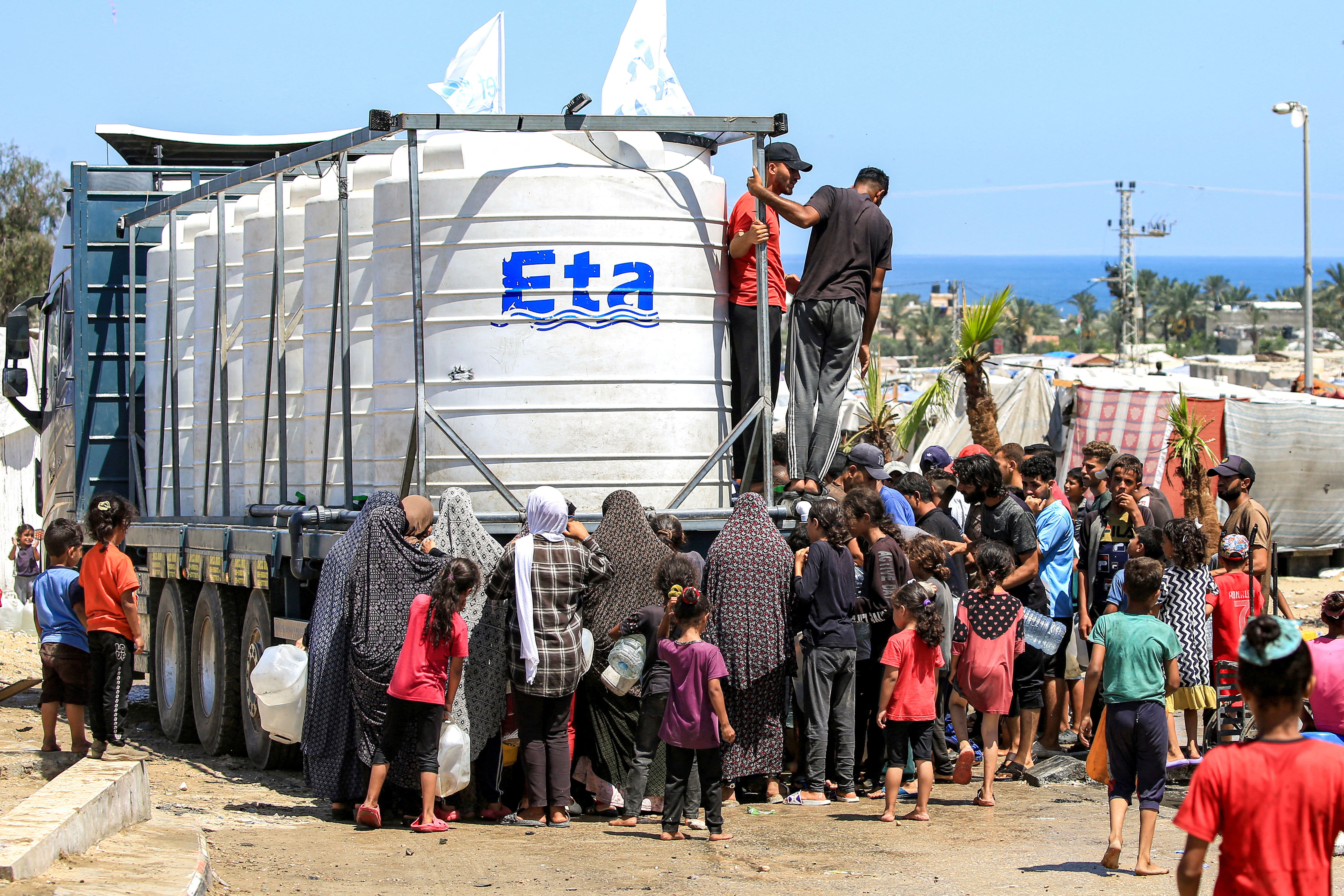 People gather to fill up their water containers from a truck loaded with water cisterns in Rafah in the southern Gaza Strip