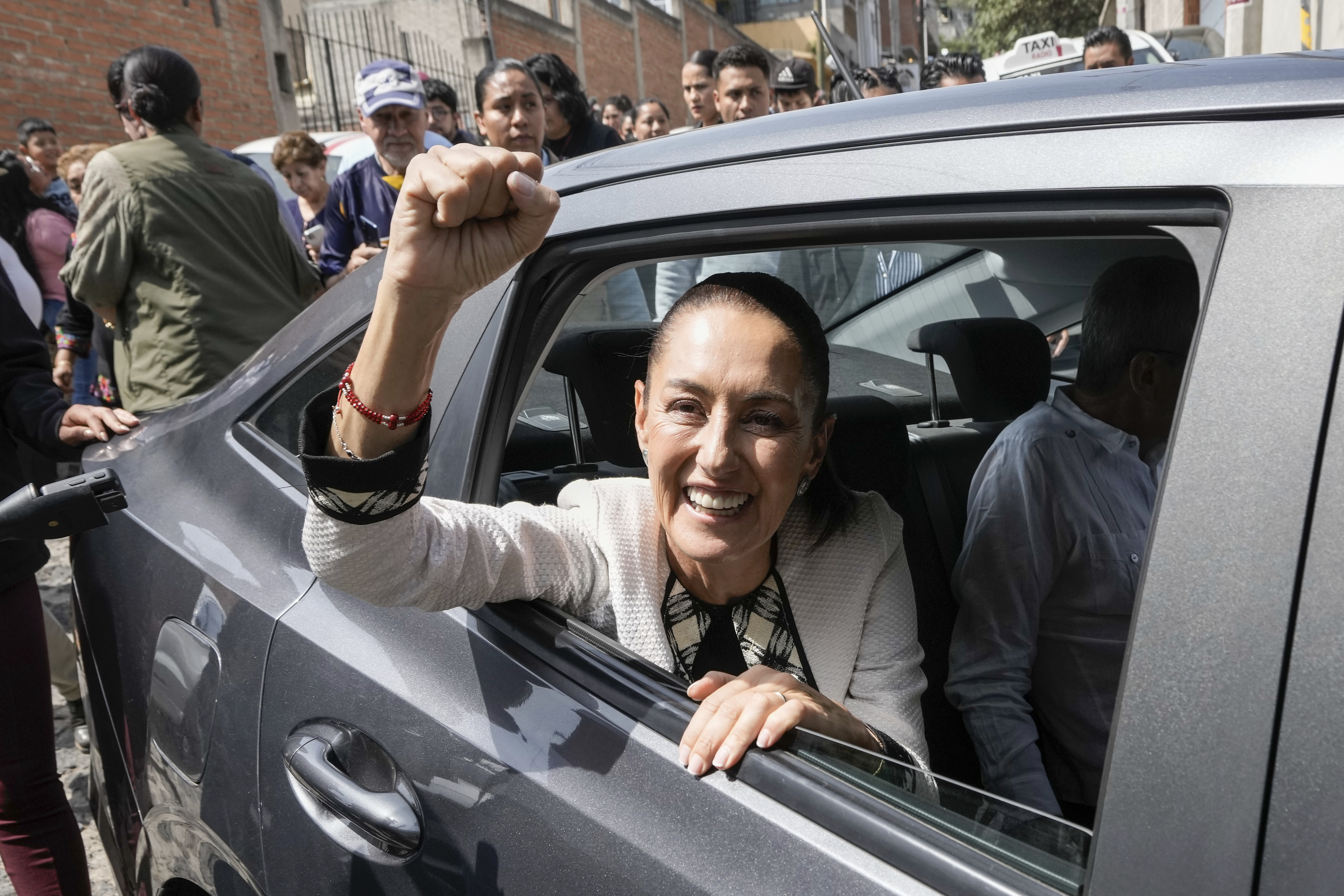 Claudia Sheinbaum pumps her fist as she acknowledges the crowd from the back of a car after leaving a polling station.