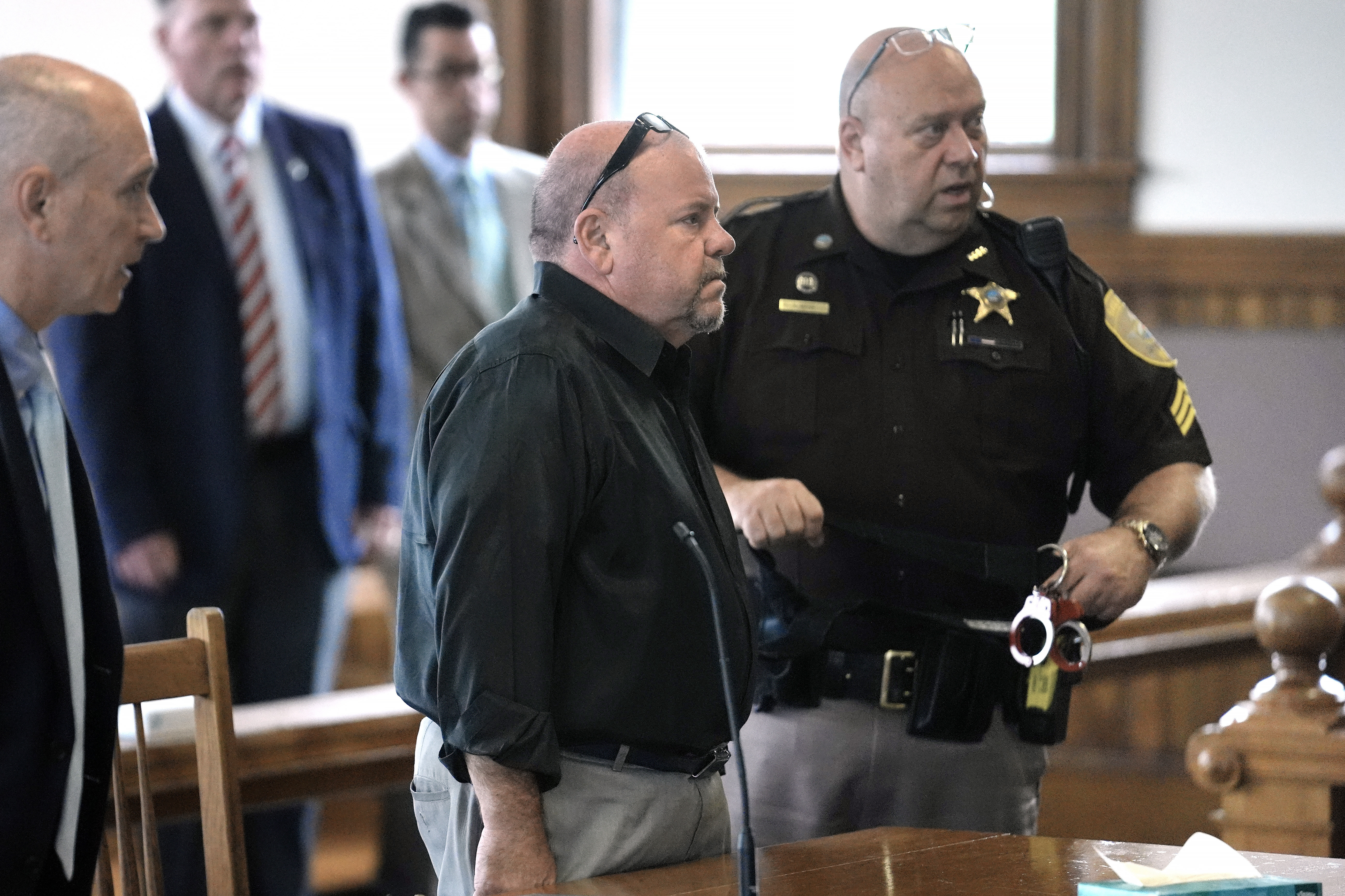 Steve Kramer stands in a courtroom, surrounded by a lawyer and a law enforcement officer.