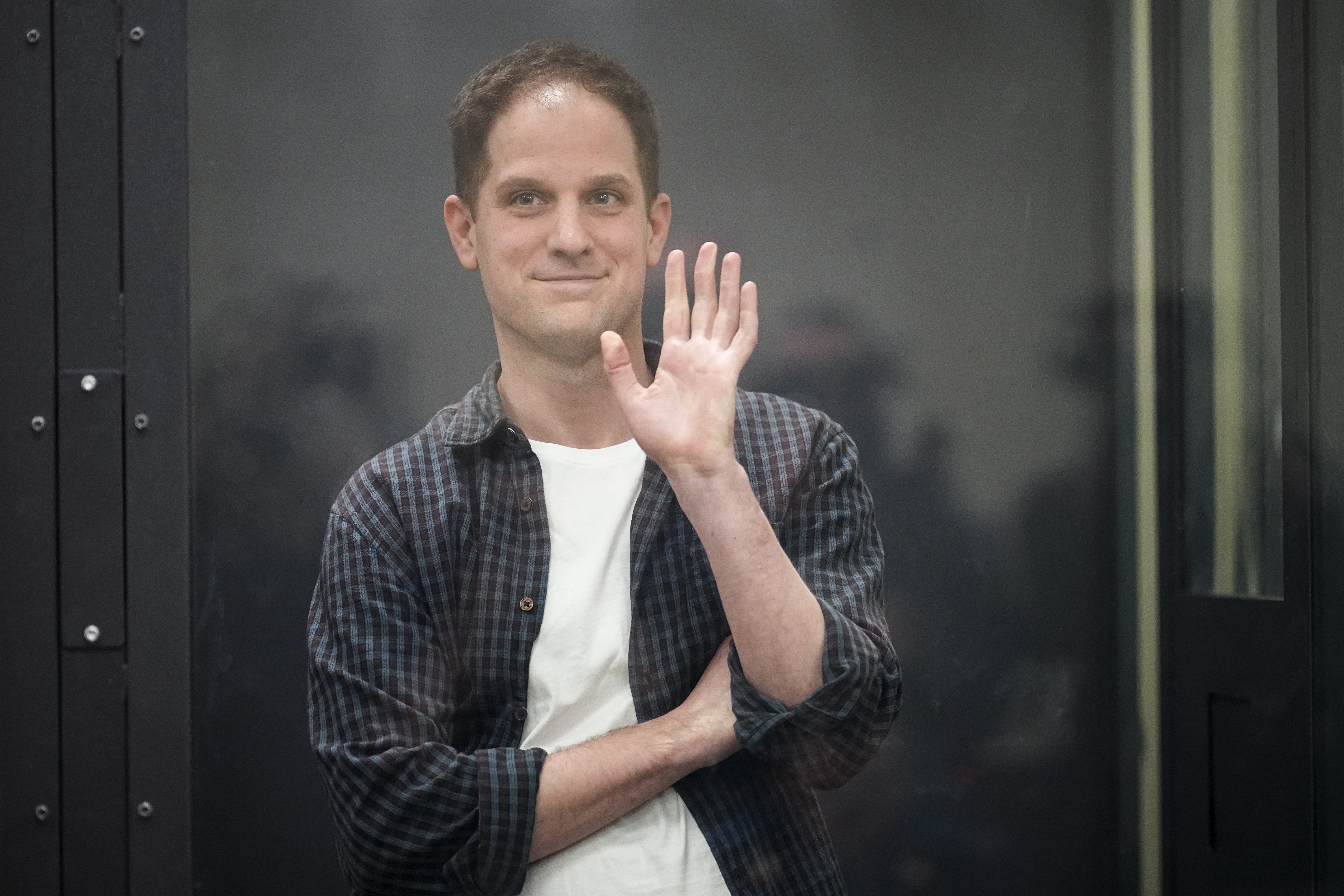 Evan Gershkovich in a glass-walled dock in a Moscow court. He is waving.