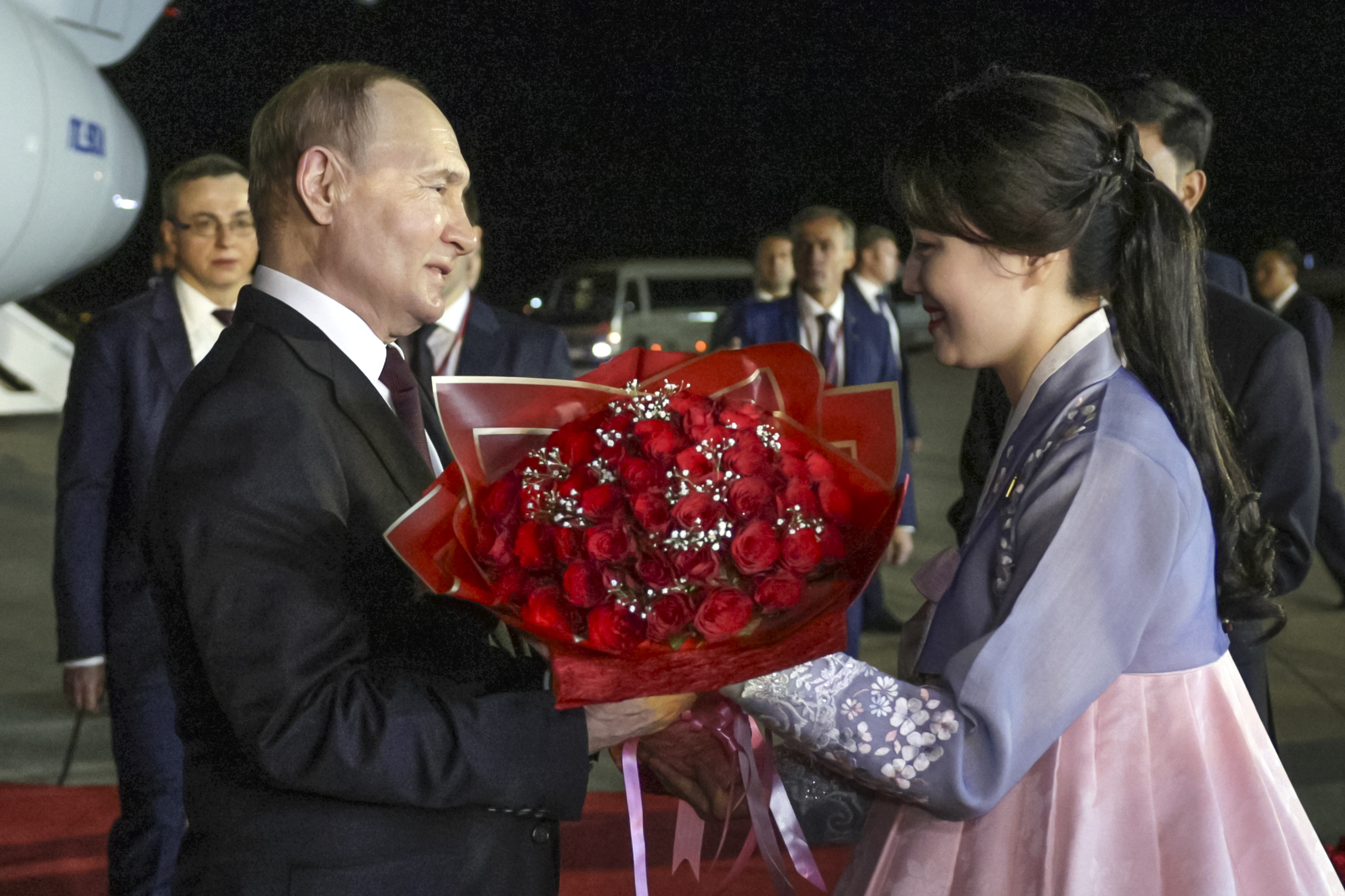 A woman in a traditional Koran hanbok gives Vladimir Putin a bouquet of red roses