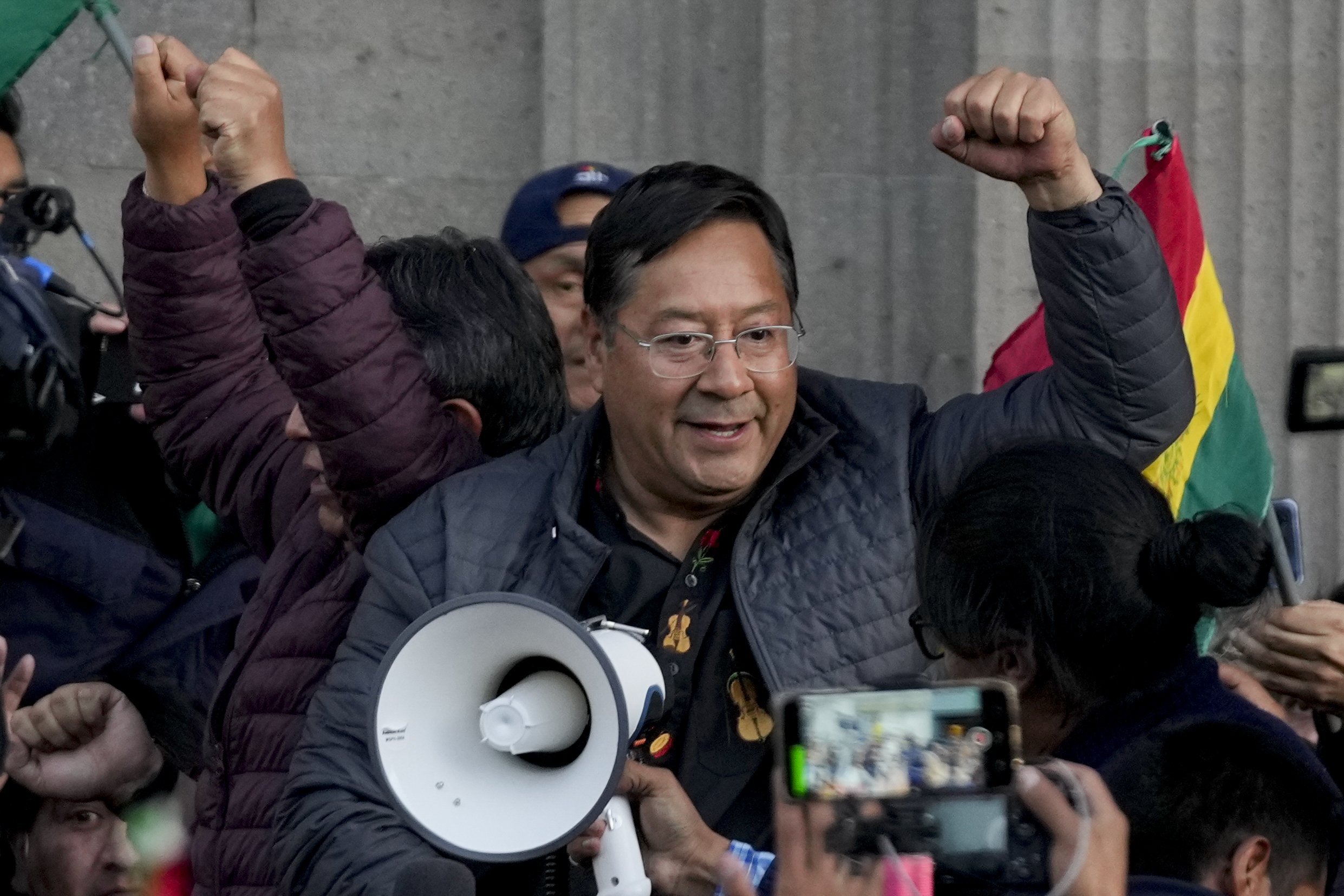 Bolivian President Luis Arce raises a clenched fist surrounded by supporters and media, outside the government palace in La Paz, Bolivia