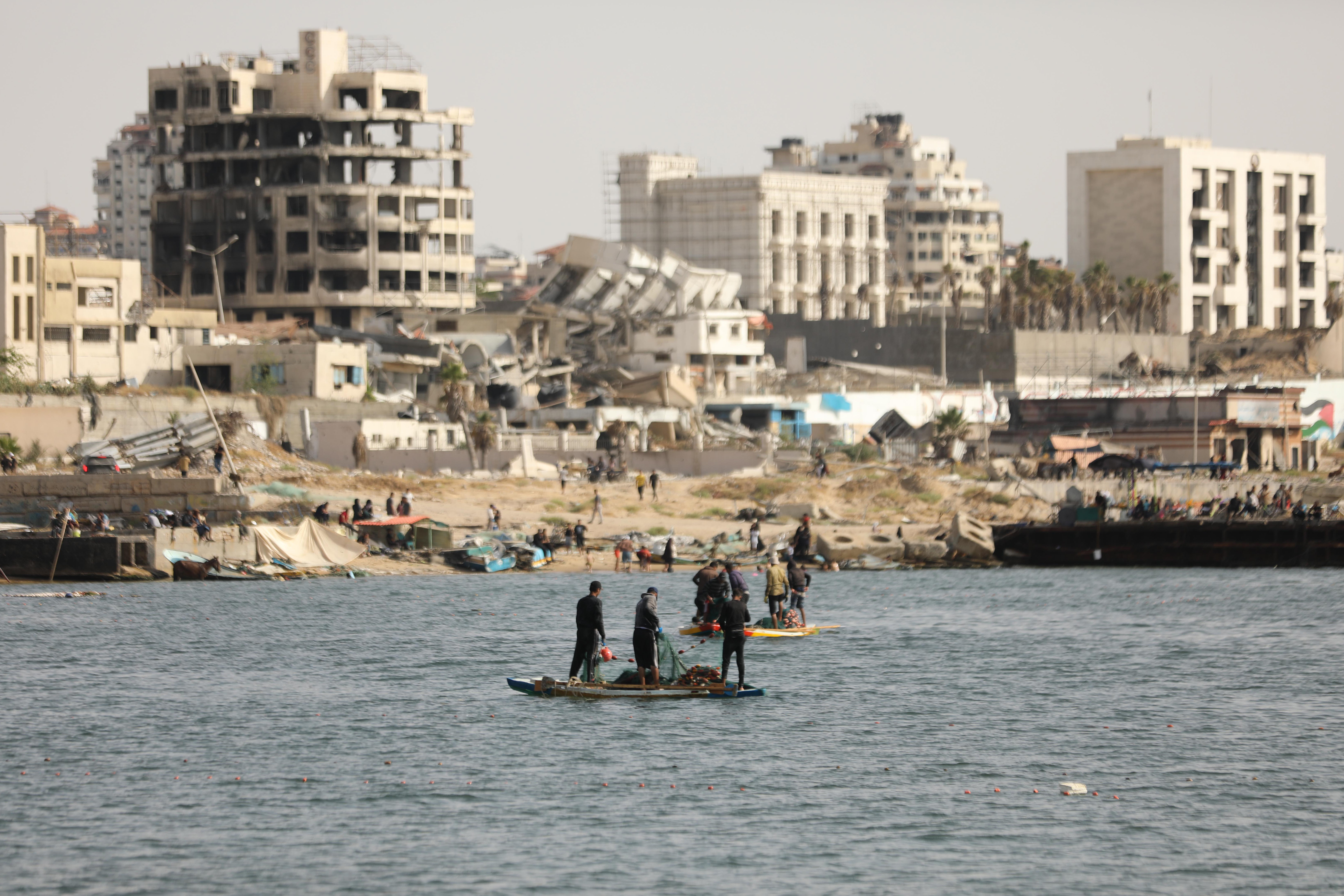 GAZA CITY, GAZA - MAY 26: Palestinian fishermen try to fish with rowing boats and fishing rods on the coast of Gaza city as damaged and destroyed buildings are seen behind in Gaza on May 26, 2024.While Israel's intense attacks on the Gaza Strip continue, some of the Palestinian fishermen who have to earn their living and bring food to their homes continue to fish, risking their lifes. (Photo by Dawoud Abo Alkas/Anadolu via Getty Images)