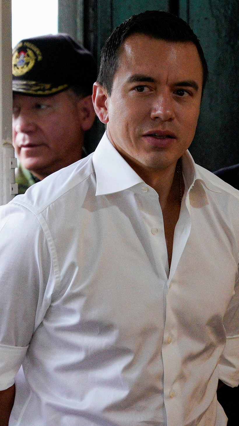 Daniel Noboa — dressed in a crisp, white collared shirt — stands near a white security gate, surrounded by officers.