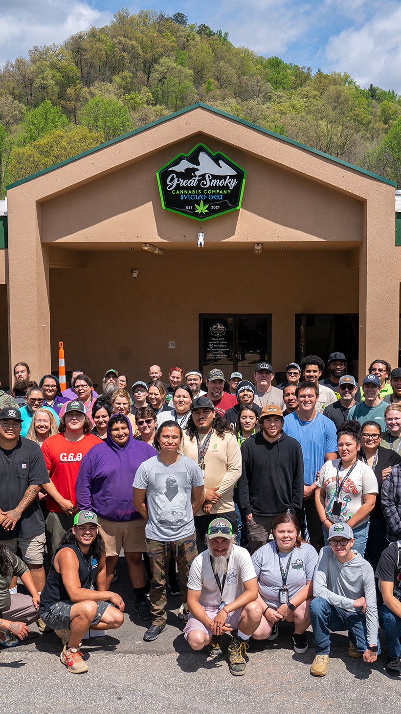 Employees and members of the Cherokee nation gather in front of the Great Smoky Cannabis Company, a brown single-story building.